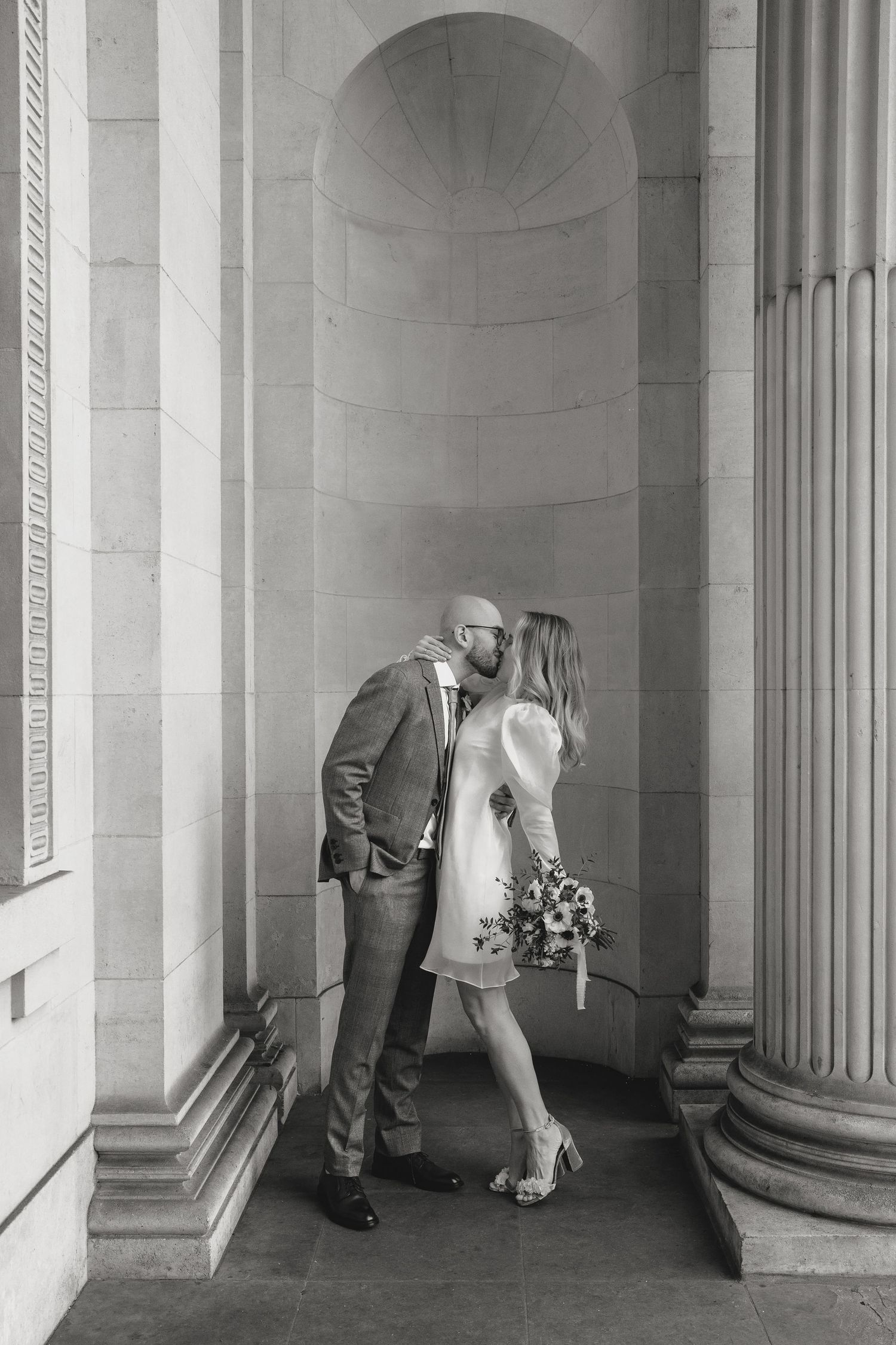 Artistic black and white wedding portraits between classical stone columns.