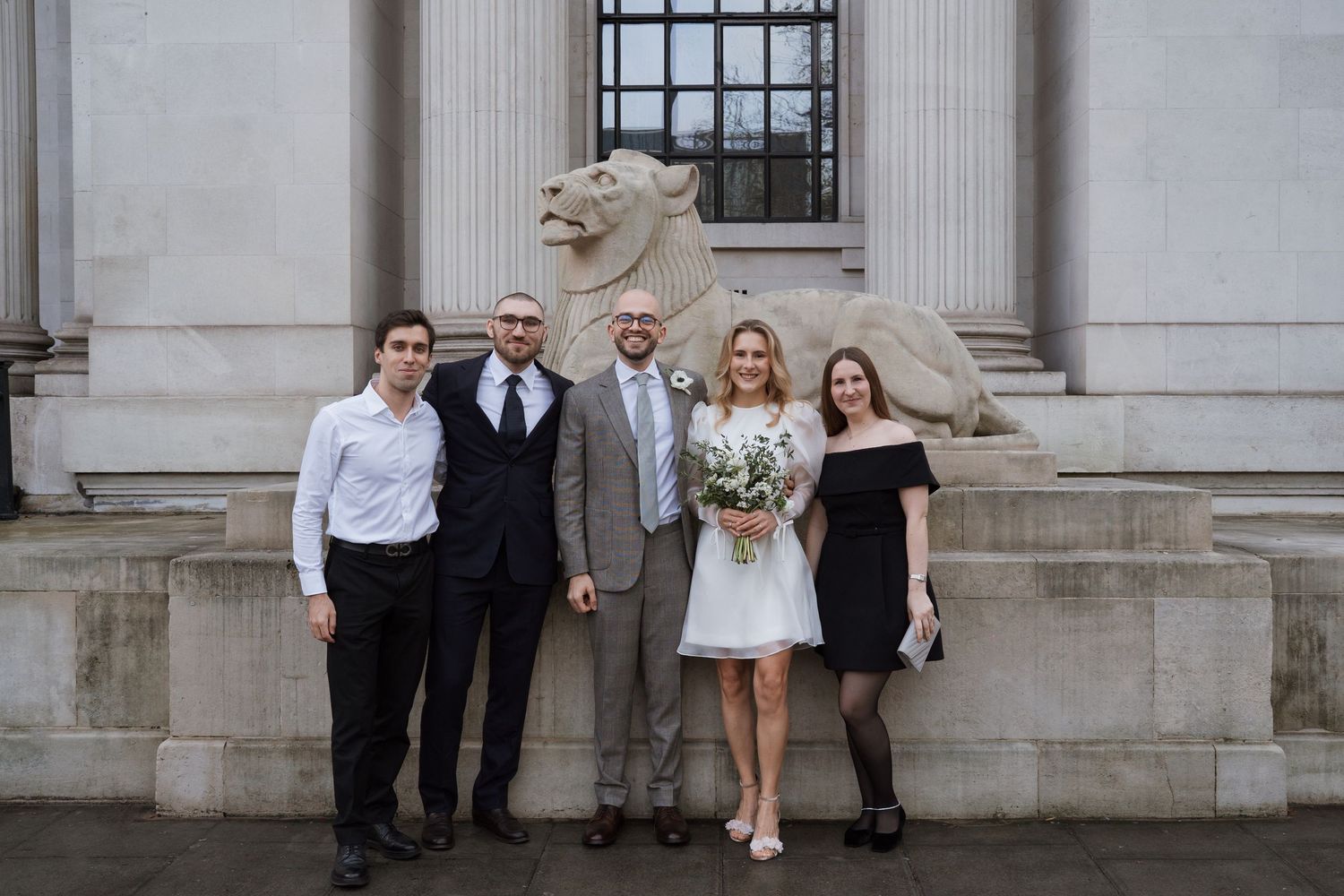A small wedding party poses together on stone steps in front of a historic building.