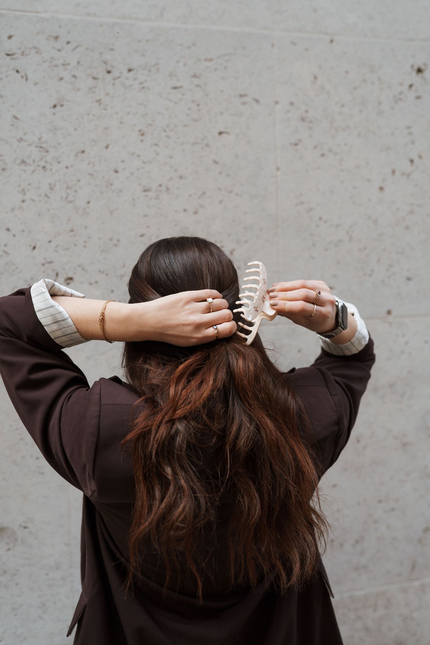 Woman with long brown hair using a white claw clip to style her hair, wearing a dark brown blazer.