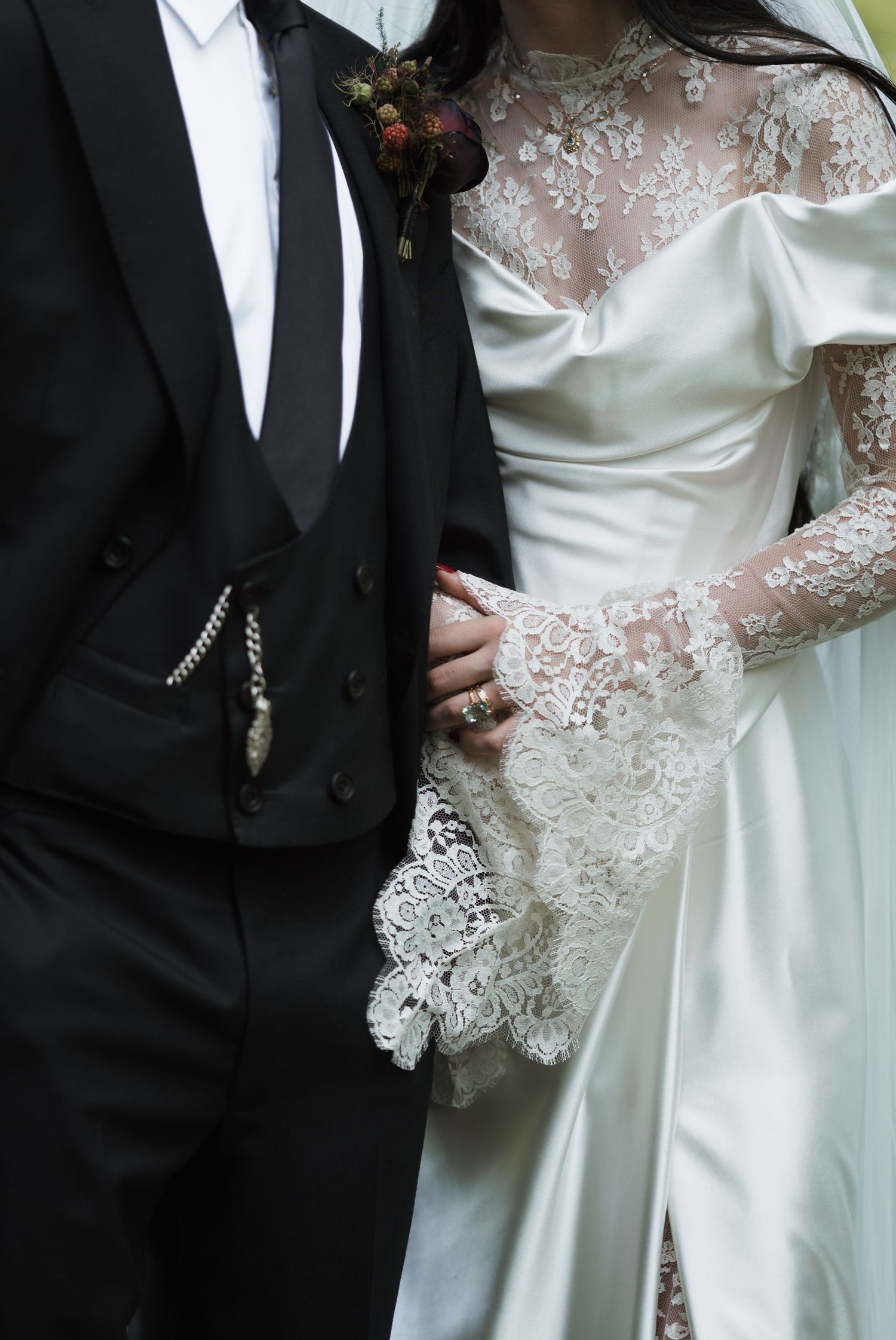 Detail shot of wedding attire showing intricate lace sleeves and classic black tuxedo.