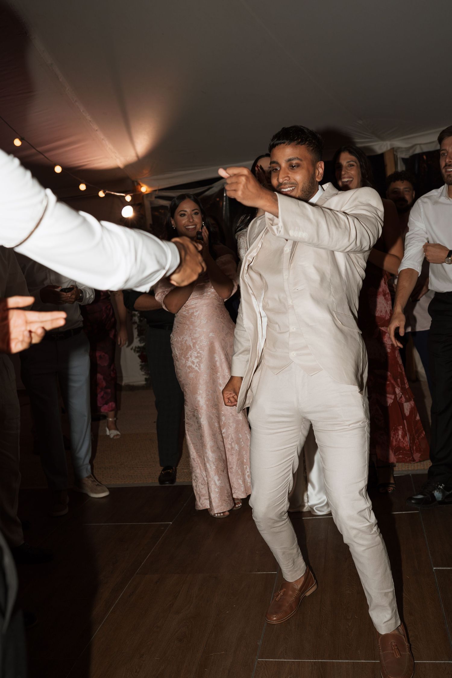 Wedding guests in white attire dance enthusiastically on a dark dance floor.