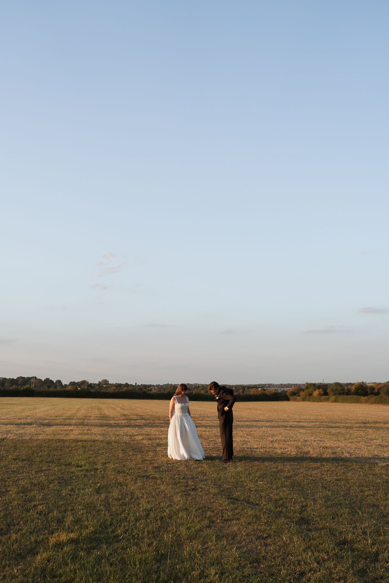 Wedding couple poses in a golden field at sunset with trees in the distance.
