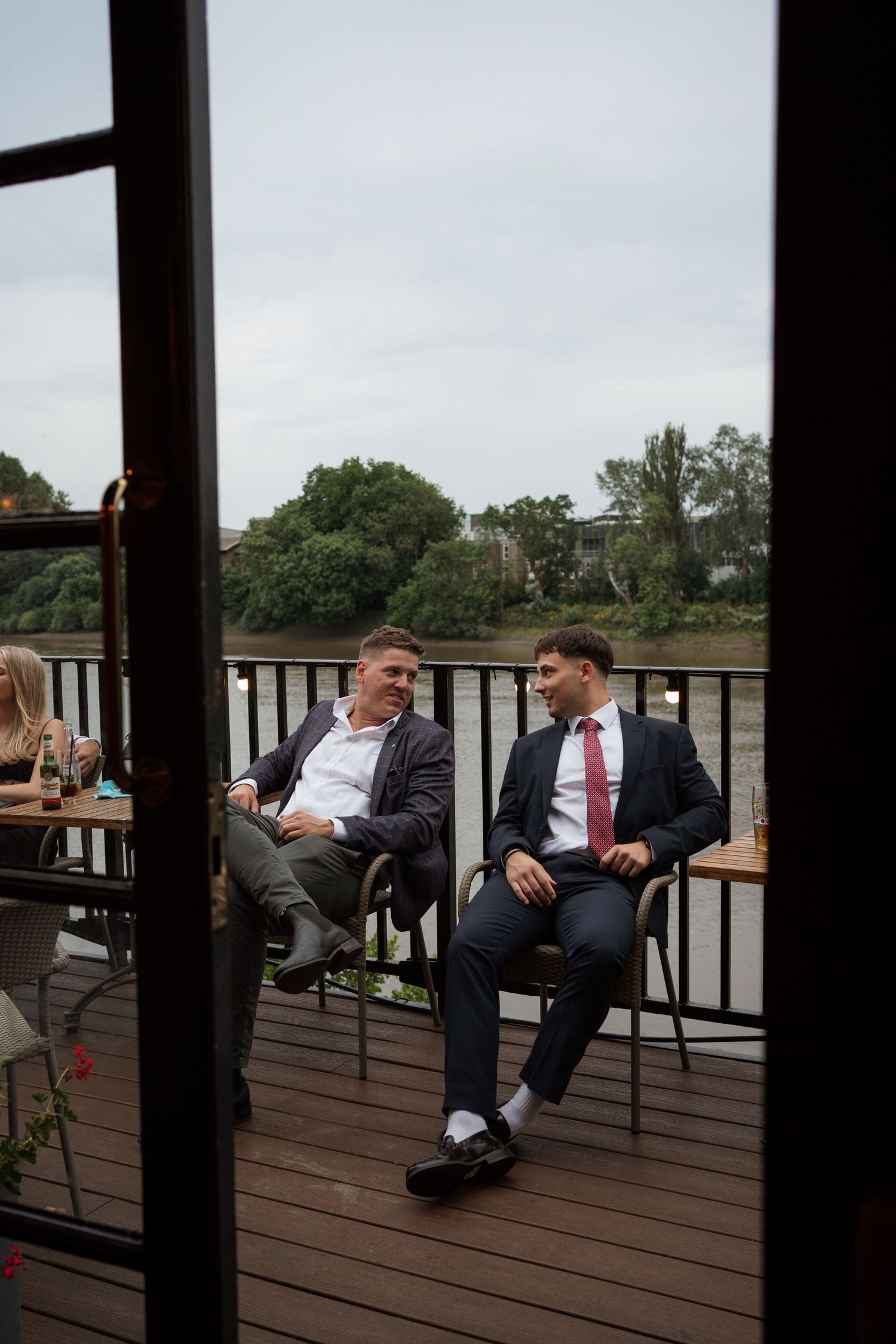 People relax on wooden deck chairs during outdoor wedding reception.