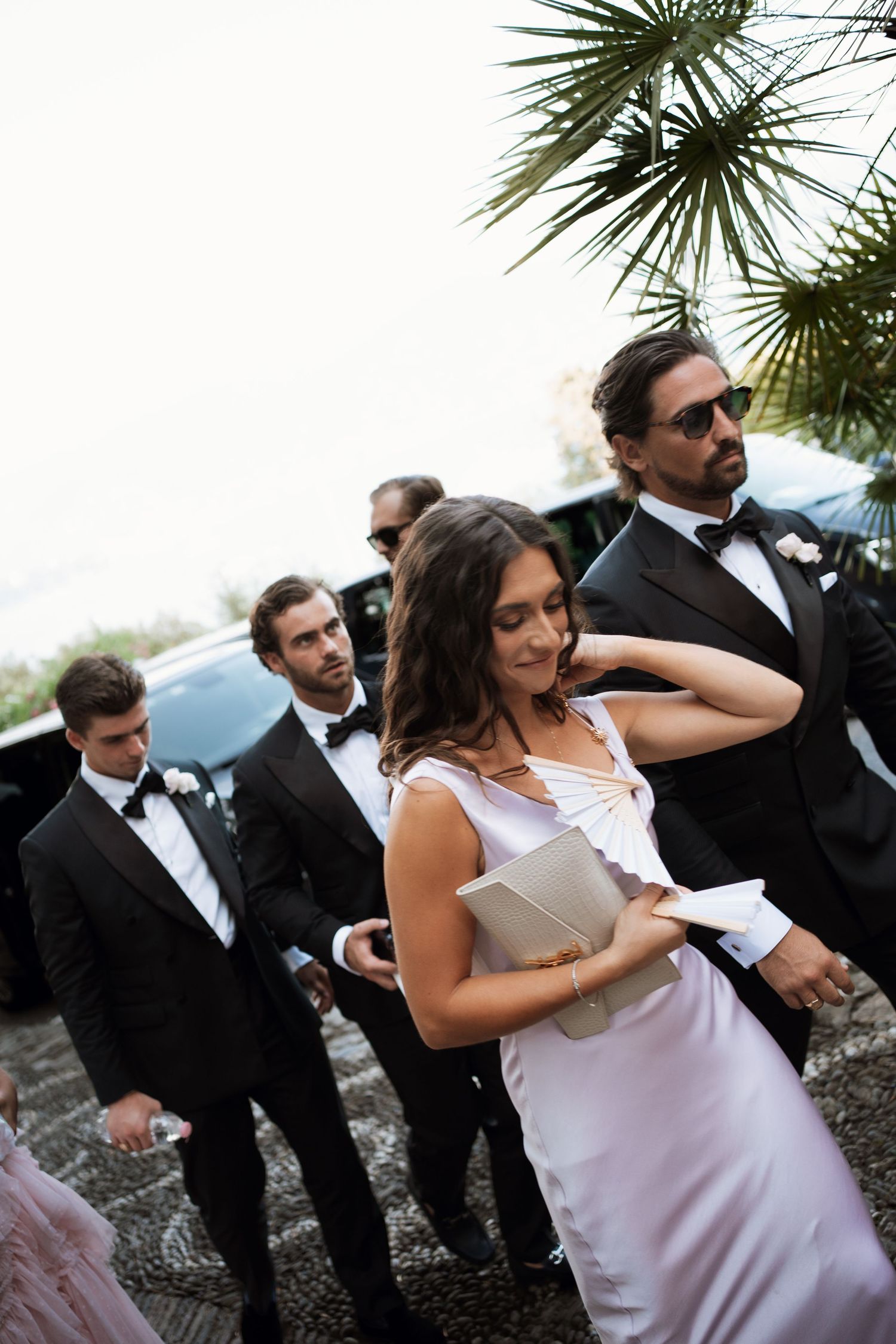 Wedding party members in formal attire walking together outdoors with palm trees in the background.