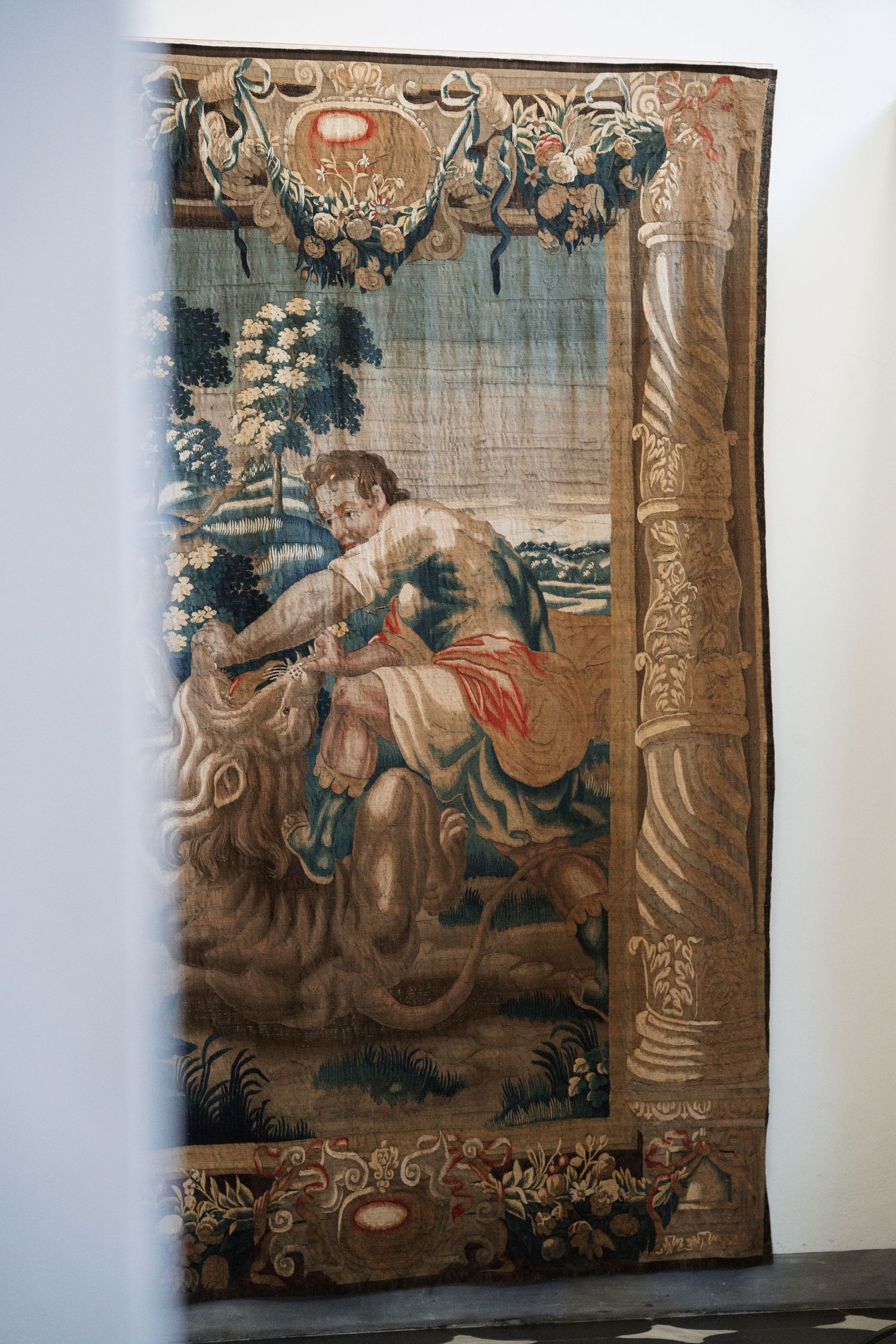 Vintage tapestry depicting classical scenes hanging on a white wall.