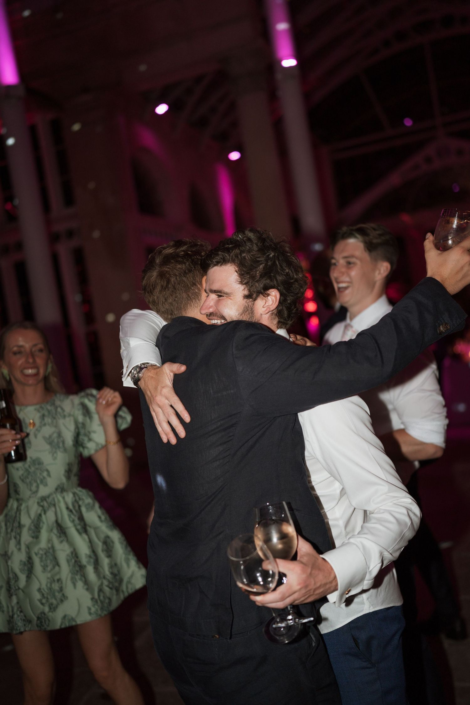 Party guests embracing and celebrating on a dance floor with purple lighting.