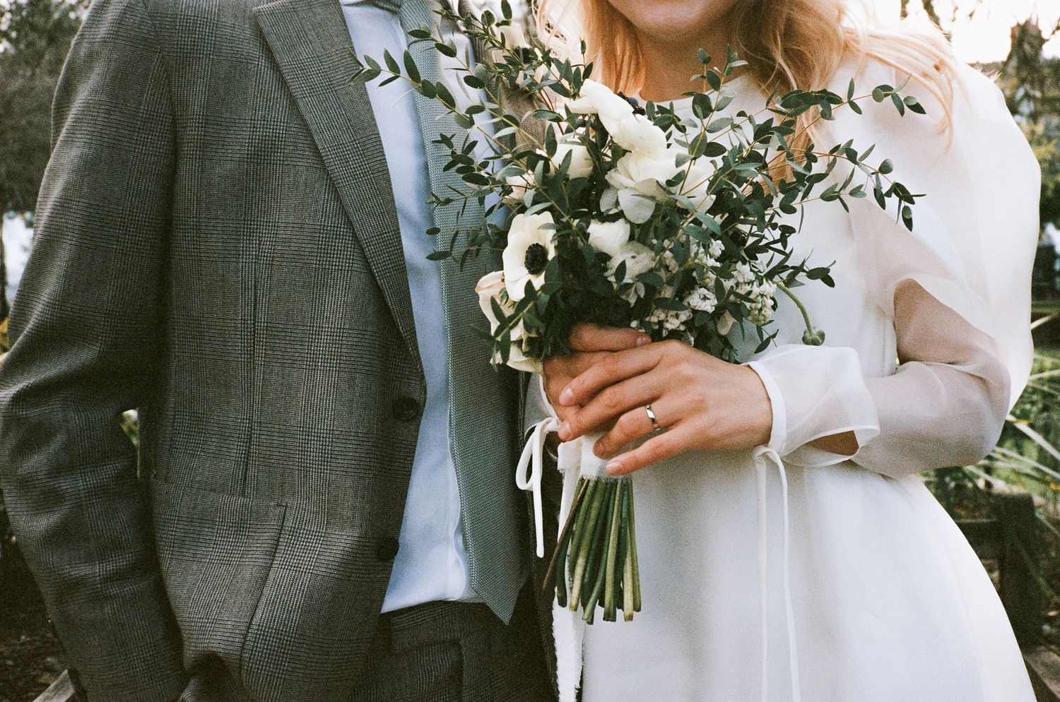 Wedding couple holding white floral bouquet against grey and white formal attire.