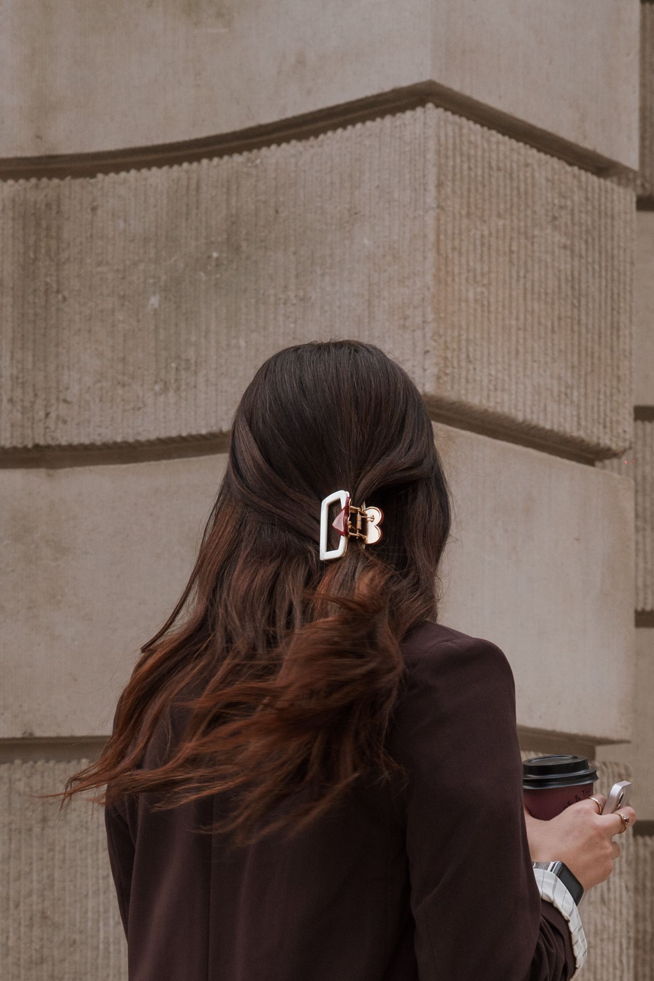 Woman with brown hair wearing a decorative hair claw clip, seen from behind near a stone building.
