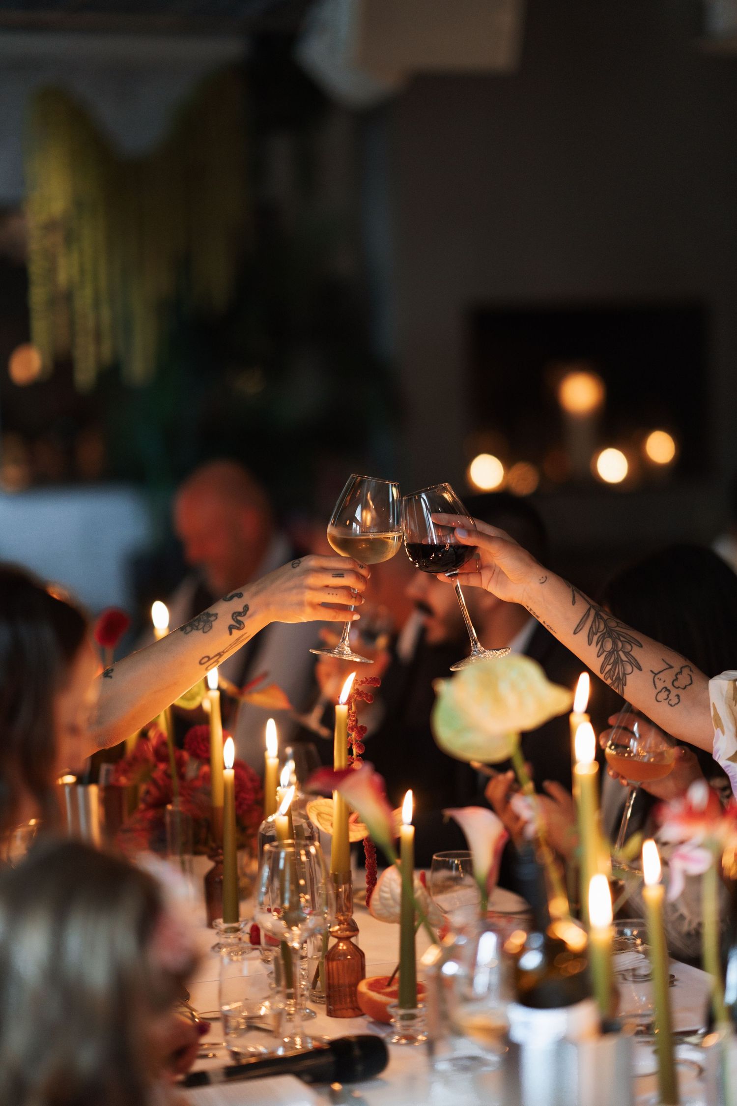 Candlelit dinner table with wine glasses and guests toasting in a dimly lit romantic atmosphere.