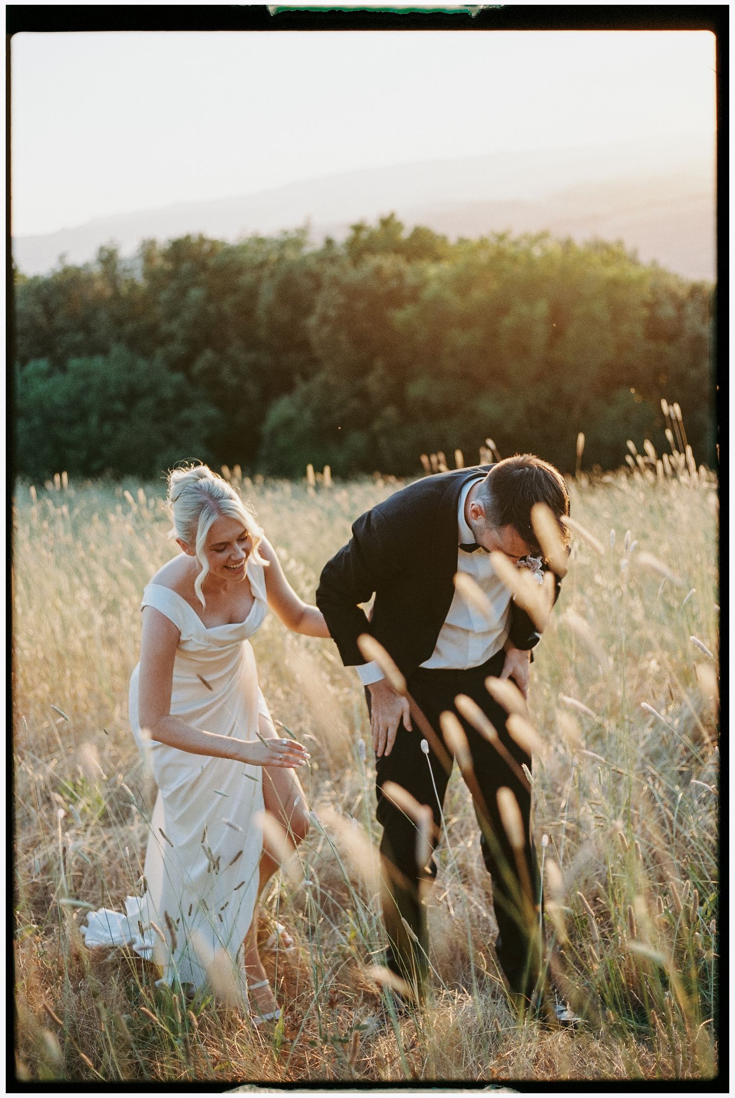 Bride and groom laughing together in golden sunlit field during outdoor wedding portrait session.