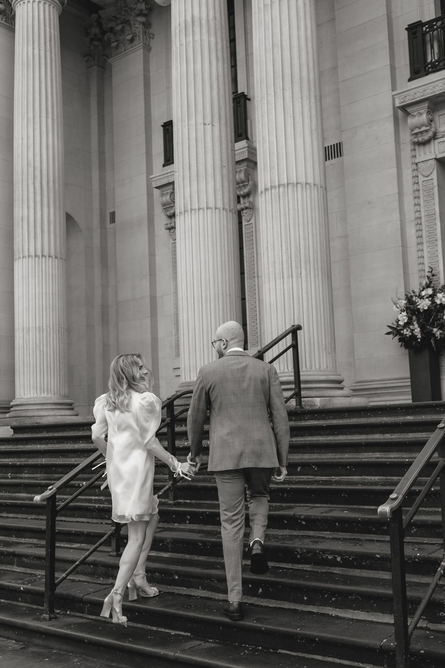 A couple ascends stone steps with classical columns in black and white photography.