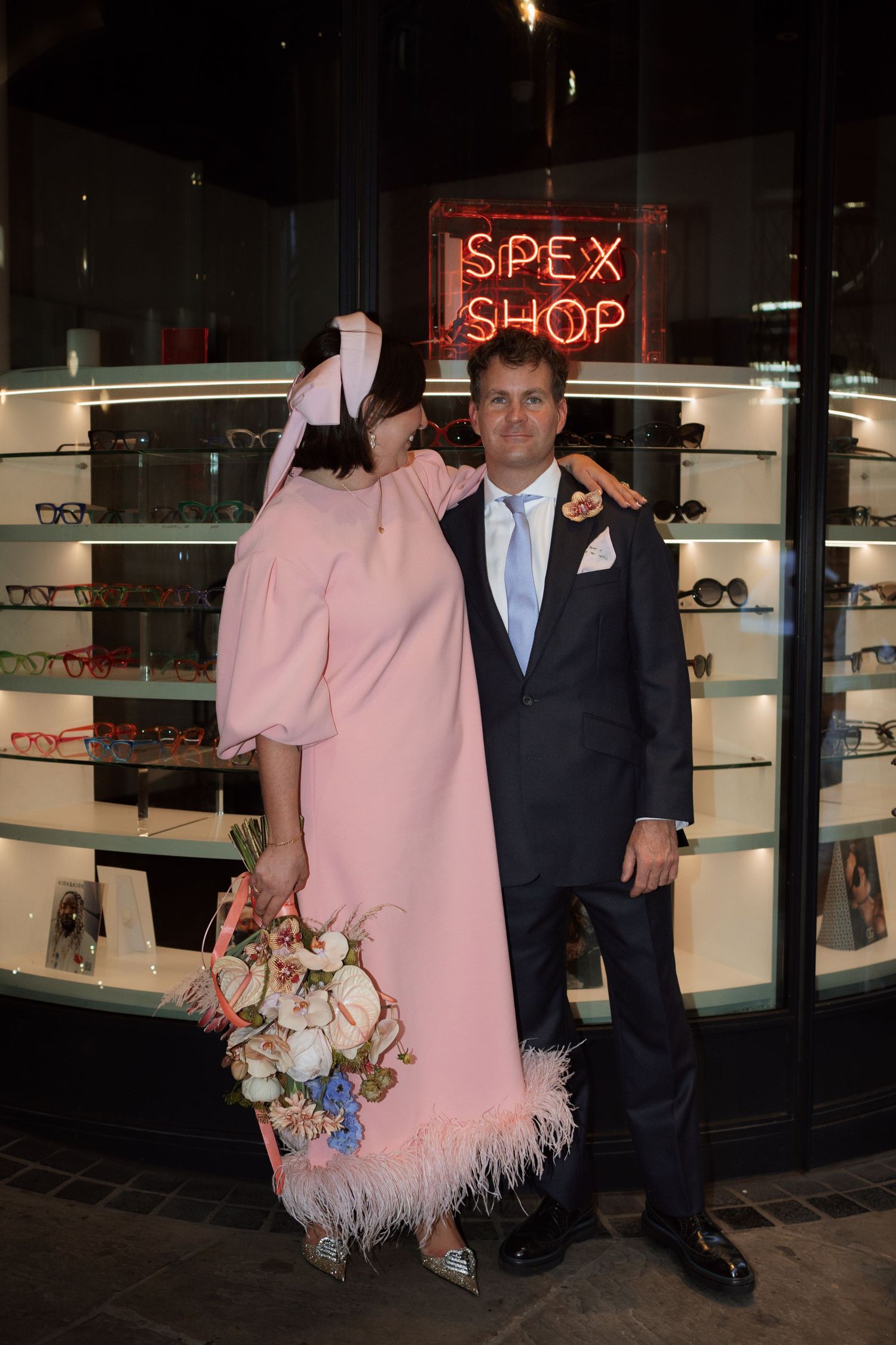 Wedding couple photographed at night outside illuminated shop window.