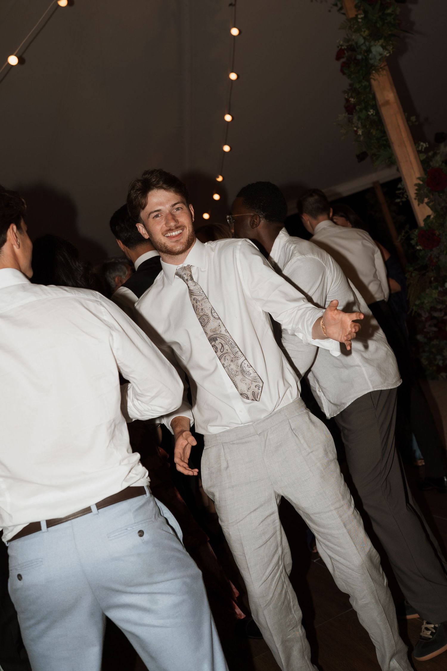 Groomsmen in light colored suits dance enthusiastically at a wedding reception.