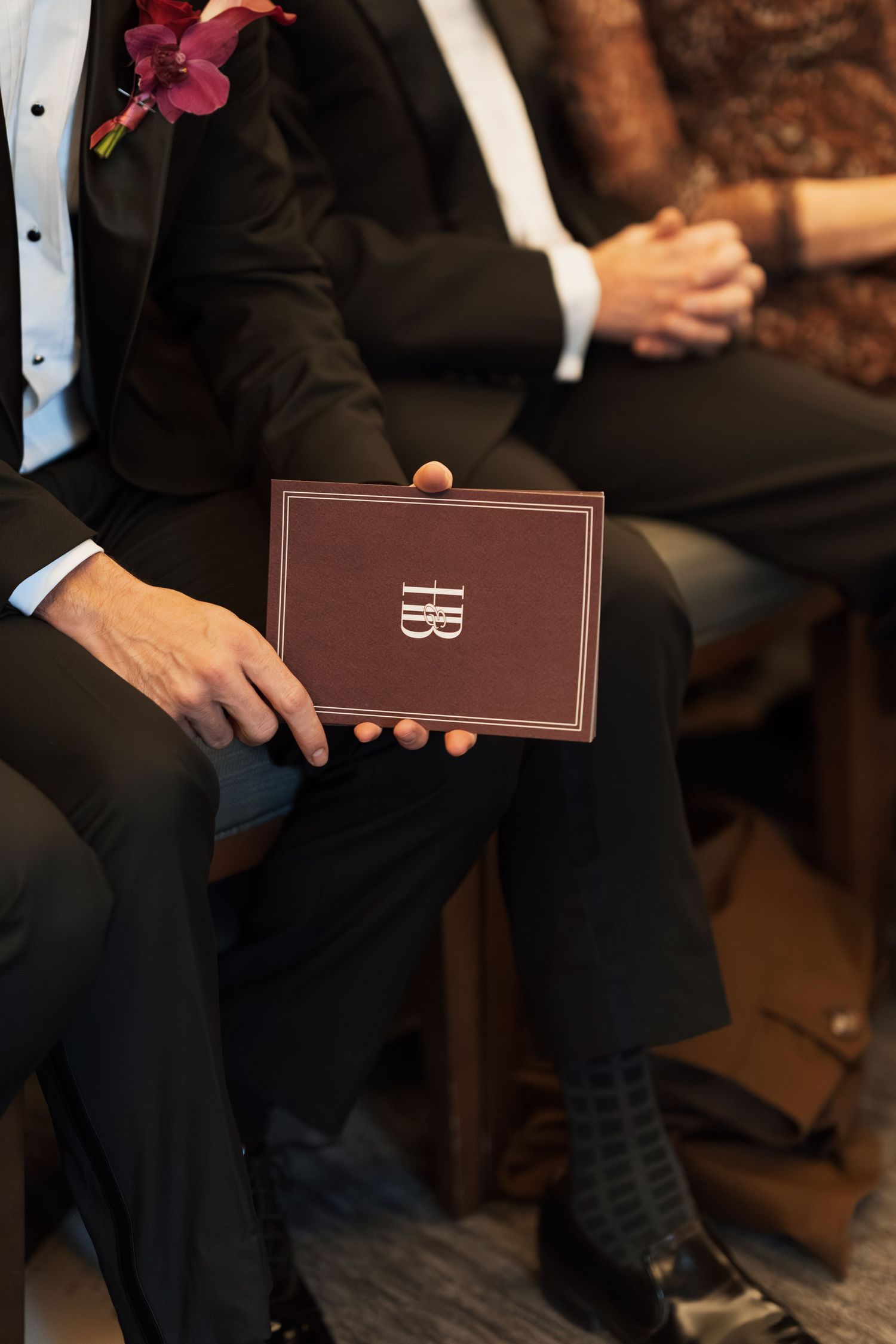 Person holding a brown leather-bound book with a boutonniere on their lapel.