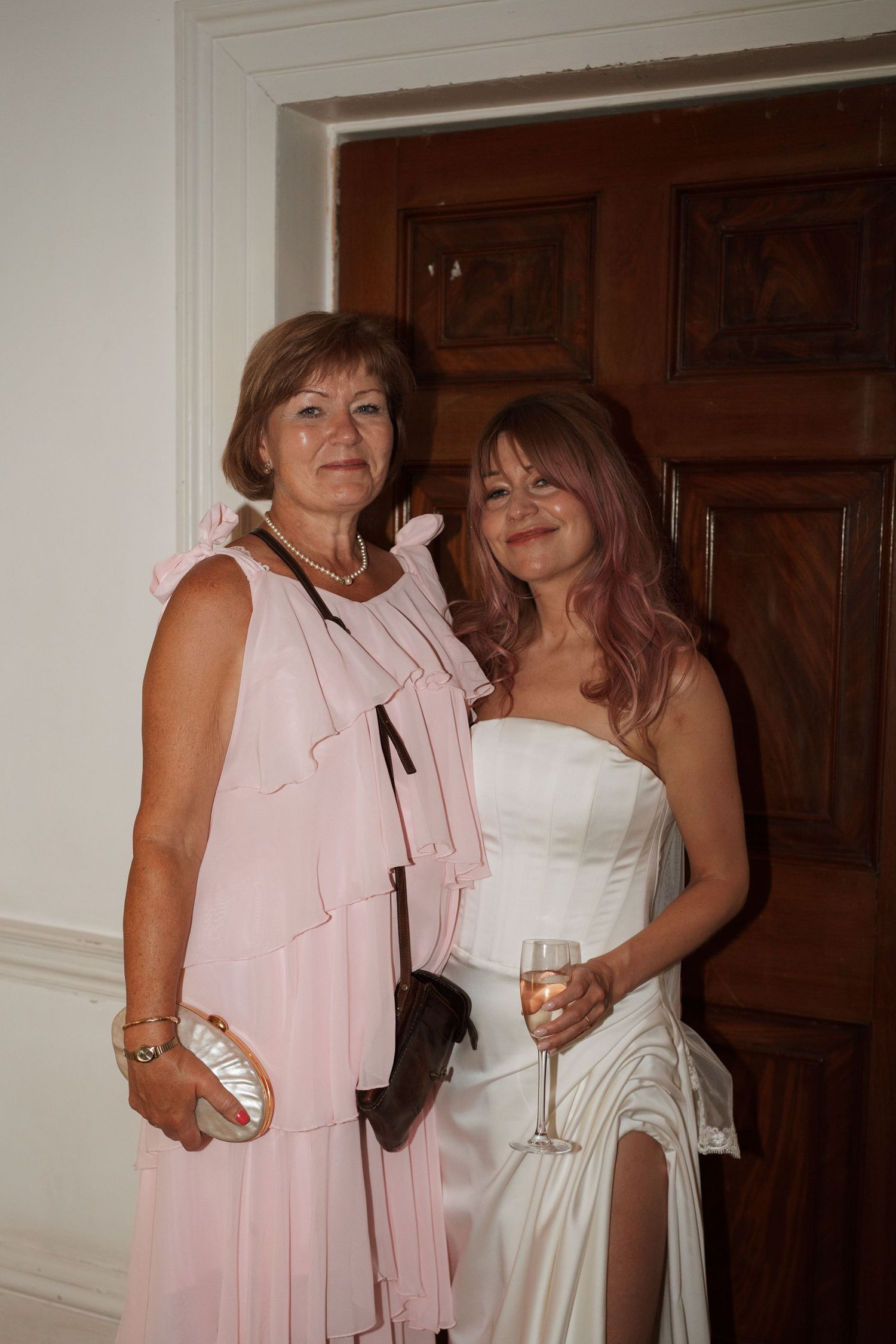 Two people in pink and white dresses embracing at a formal event.