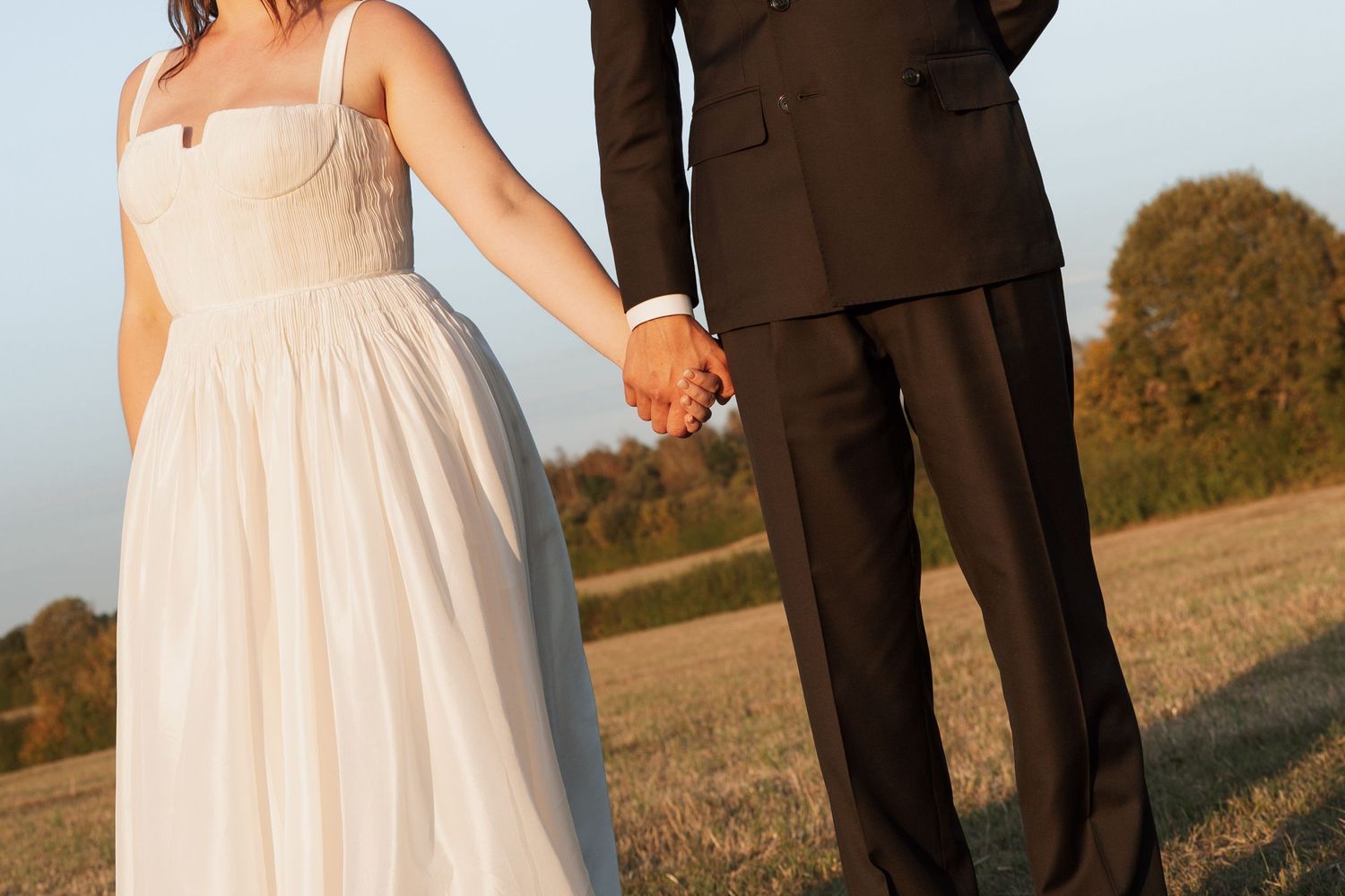 Couple in wedding attire standing together in warm evening sunlight.