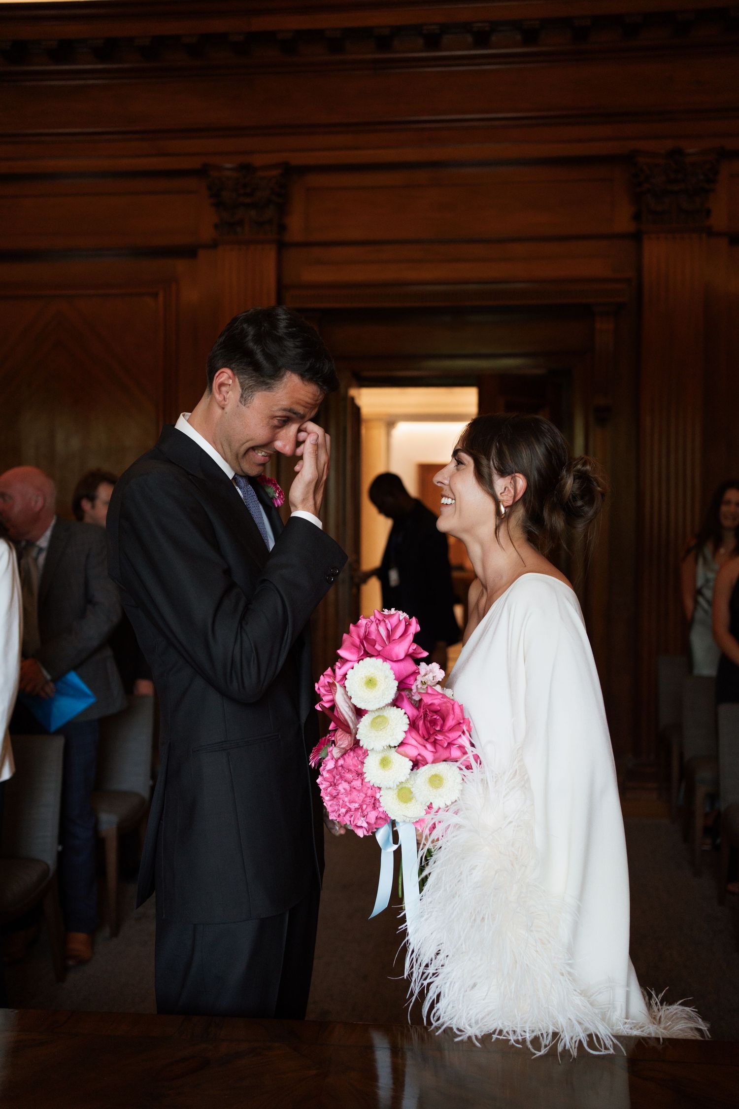 Couple in formal attire walking through ornate hallway with pink and white bouquet.