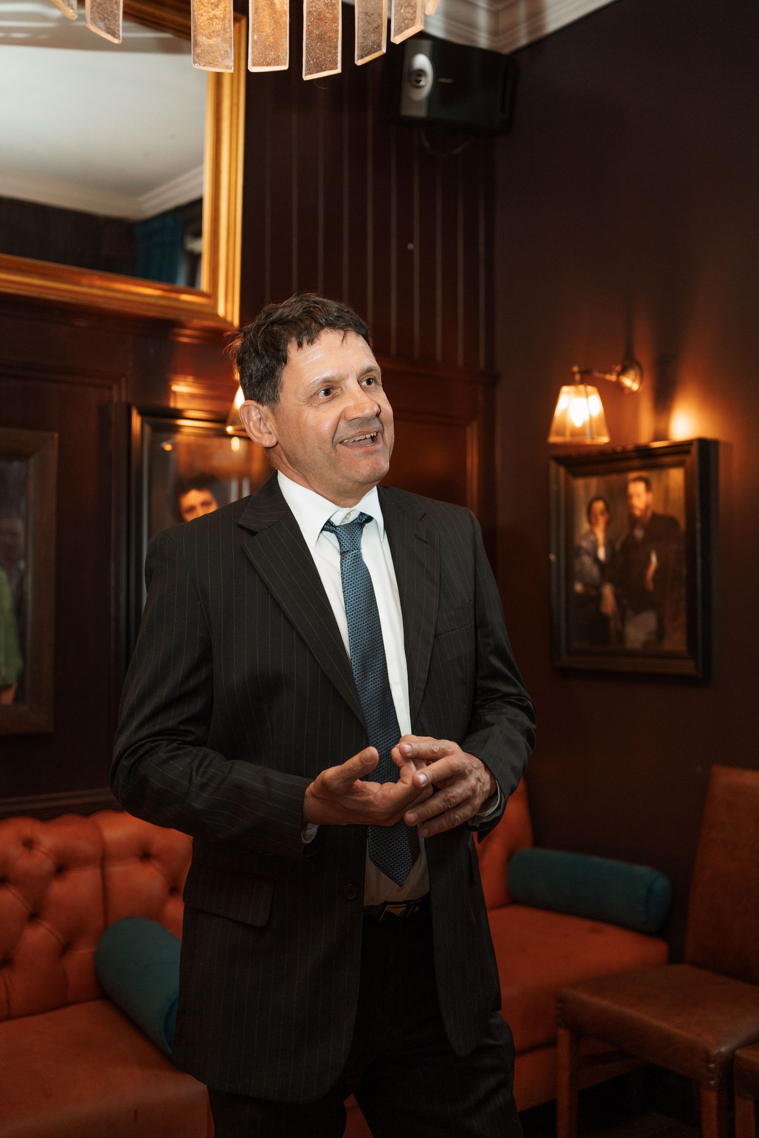 Person in formal attire stands in warmly lit elegant room with wood paneling.