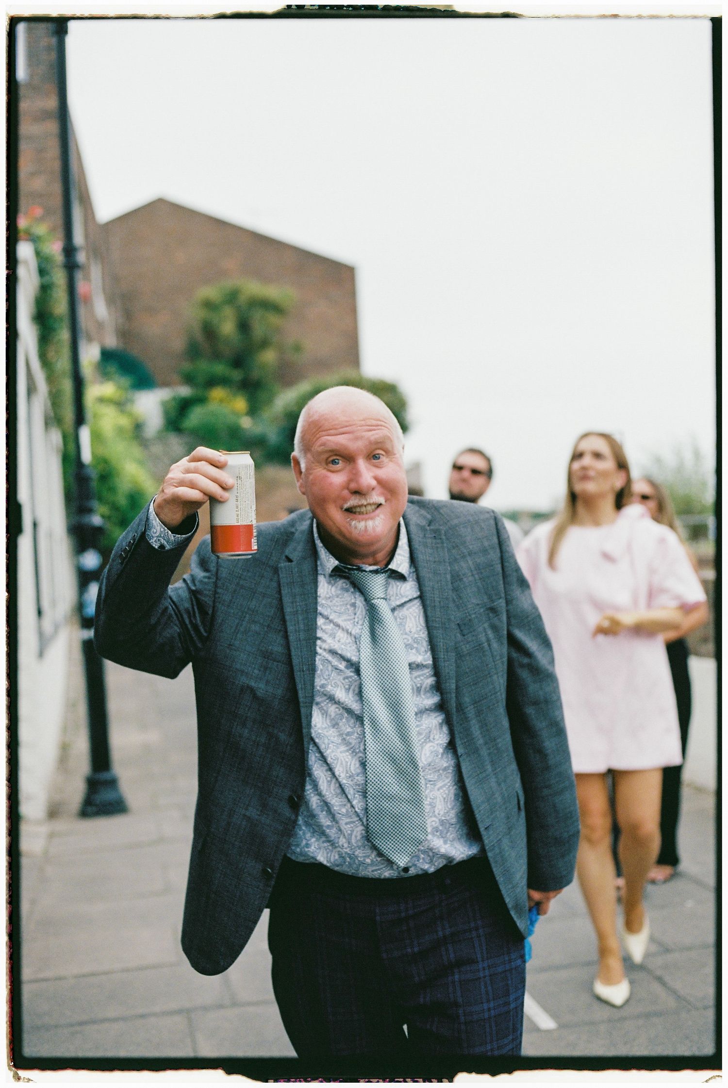 Elderly gentleman in a grey suit gesturing enthusiastically at an outdoor event.