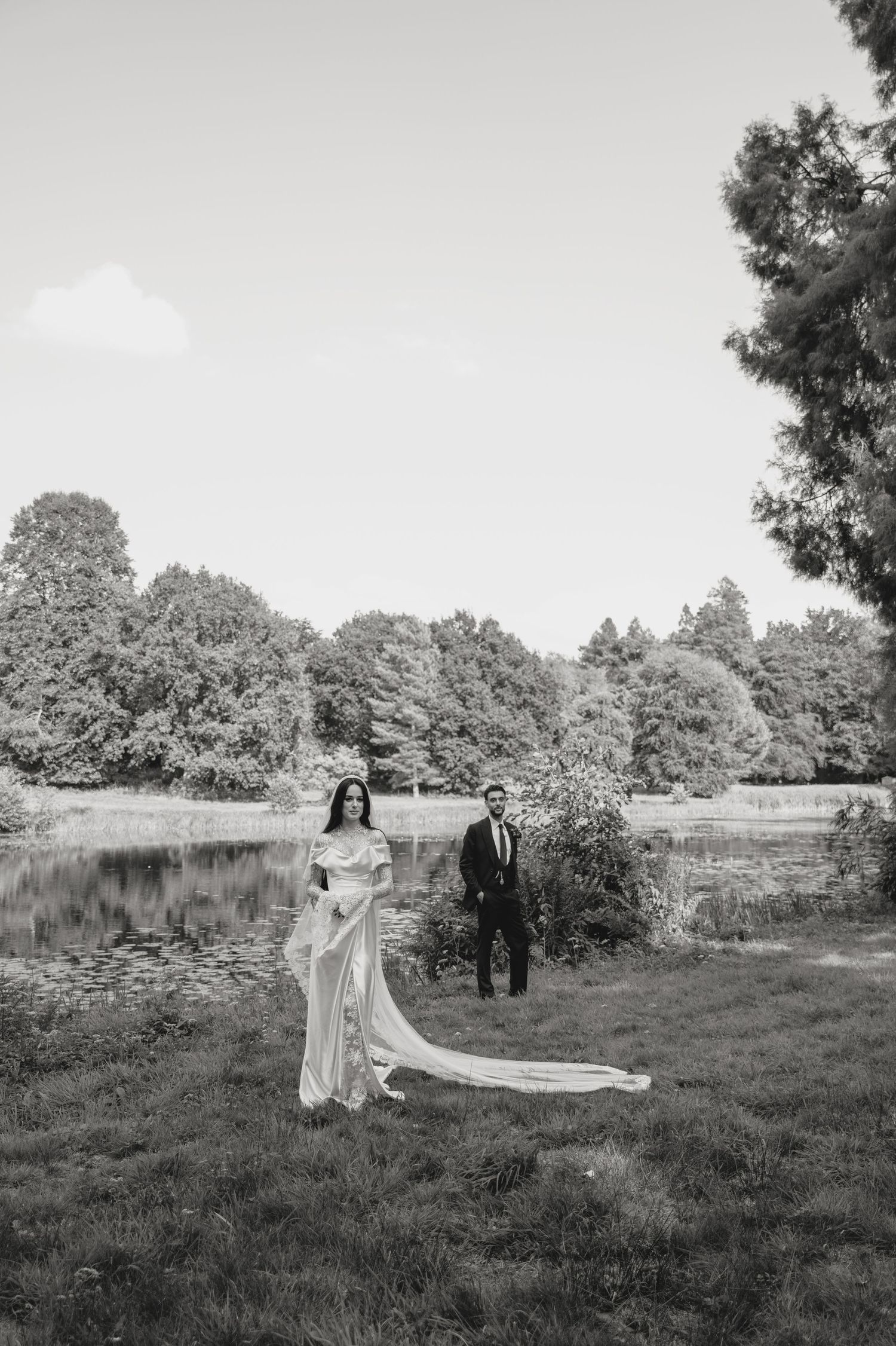 A wedding couple poses in a scenic field with flowing veil and natural landscape backdrop.
