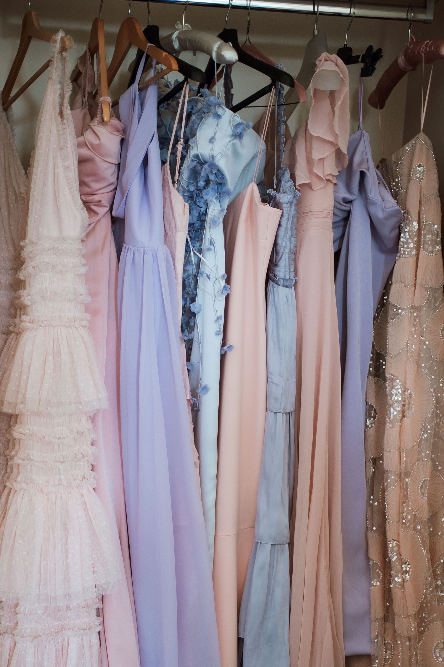 Collection of pastel bridesmaid dresses in pink, purple, and blue hanging on a rack.