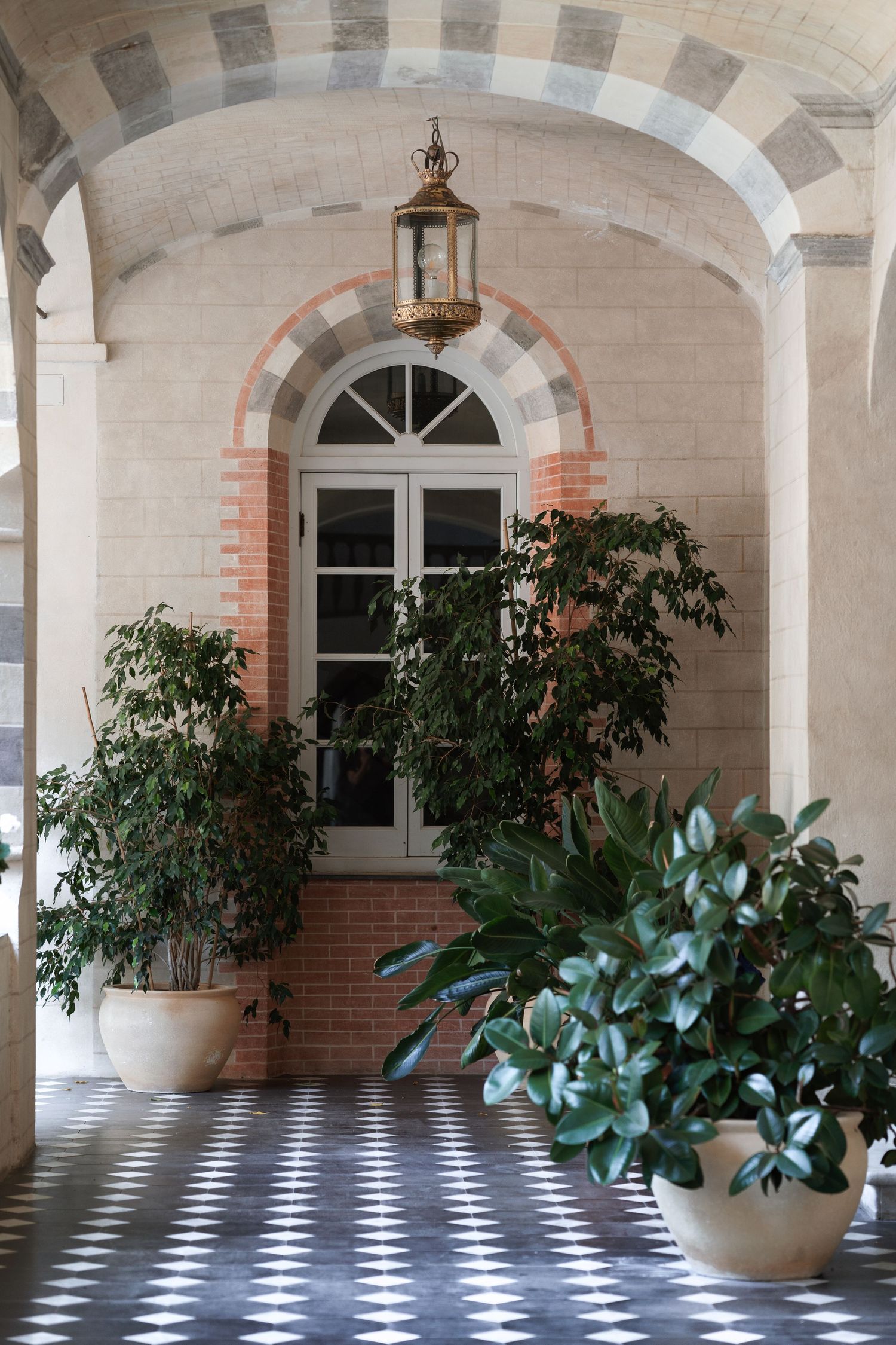 Elegant arched hallway with checkered floor and potted plants beneath a hanging lantern.
