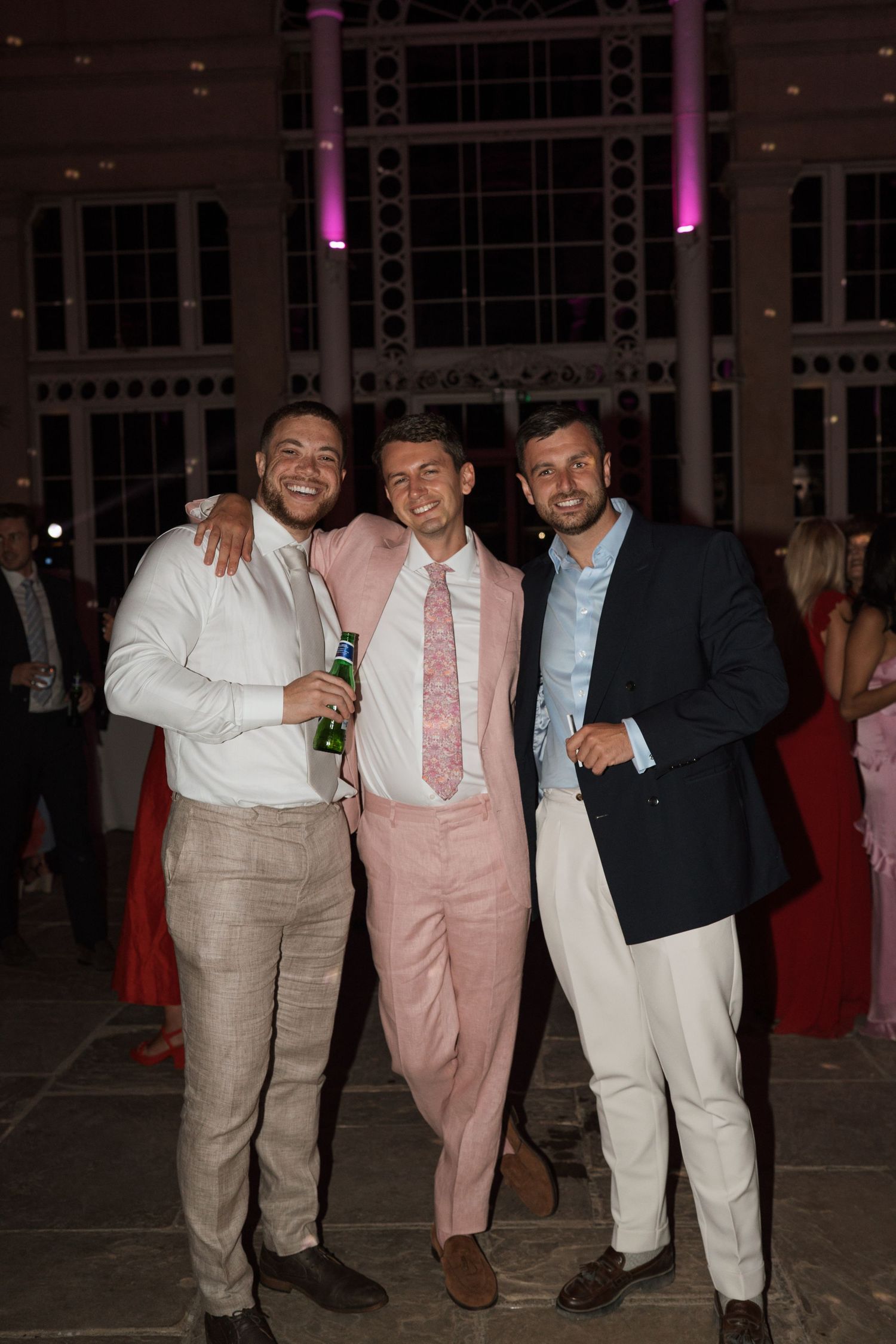 Group of friends in formal wear posing together at an event with purple lighting.