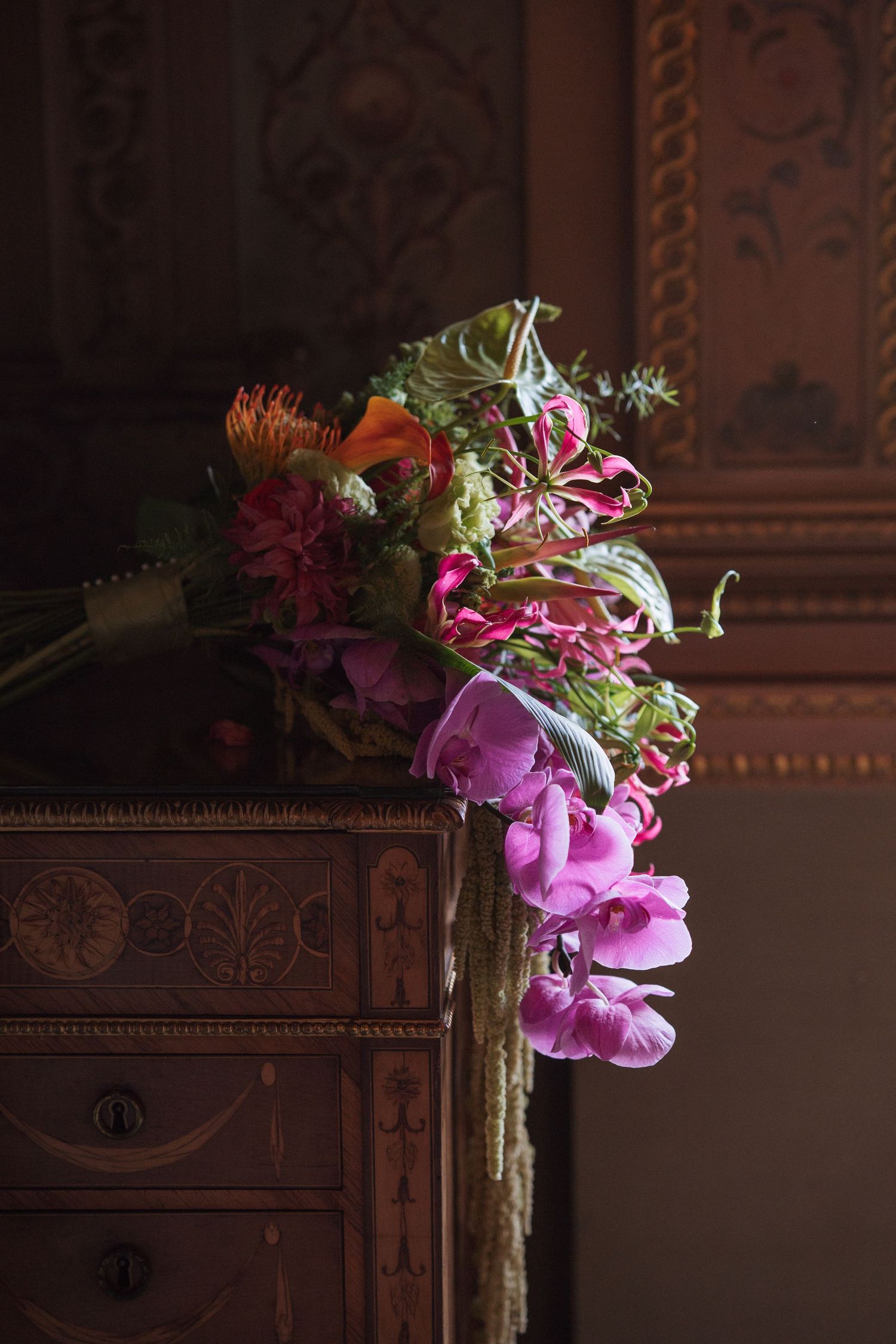Elegant floral arrangement with pink orchids and tropical flowers in dark moody lighting.
