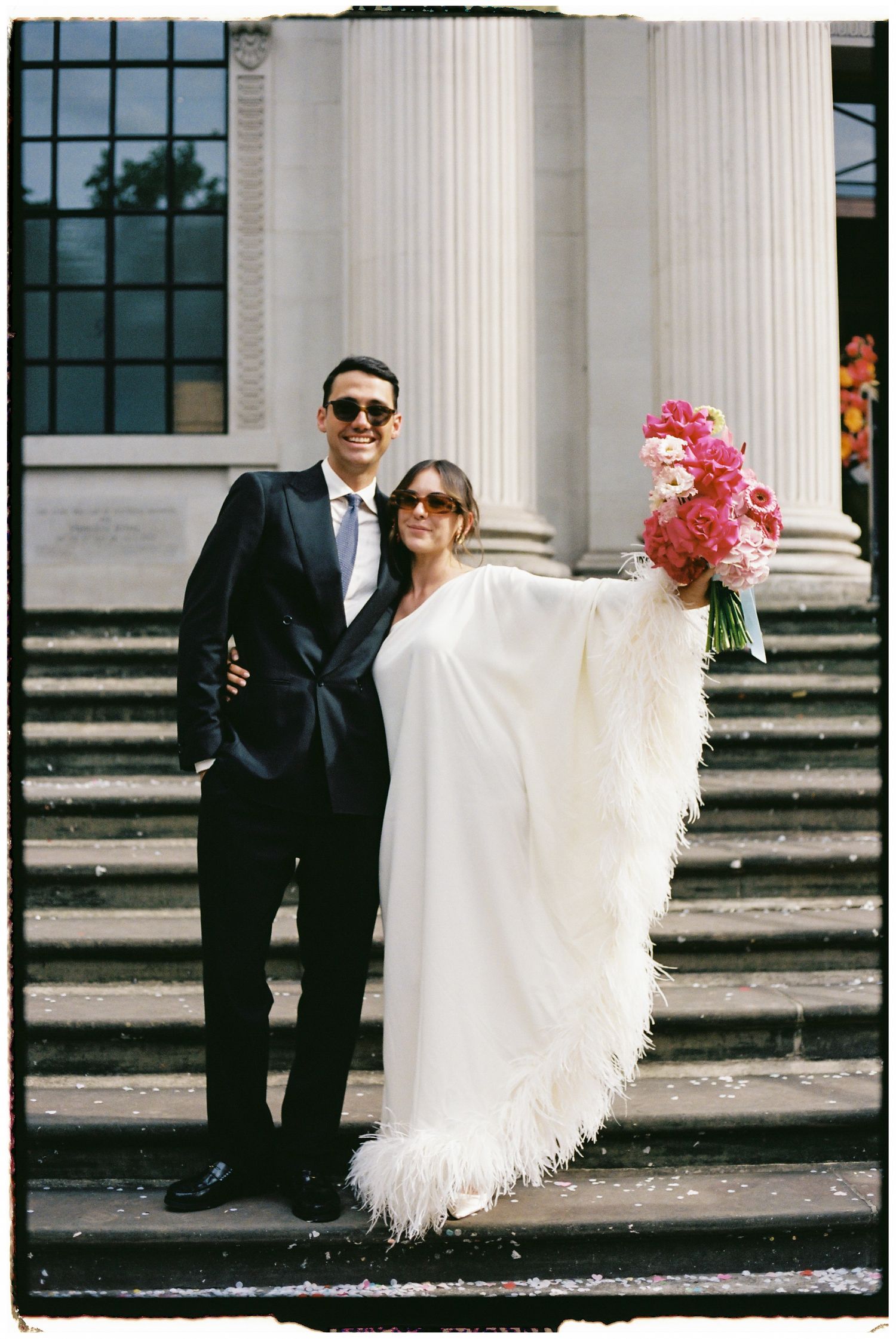 Wedding couple posing by classical white columns on stone steps.