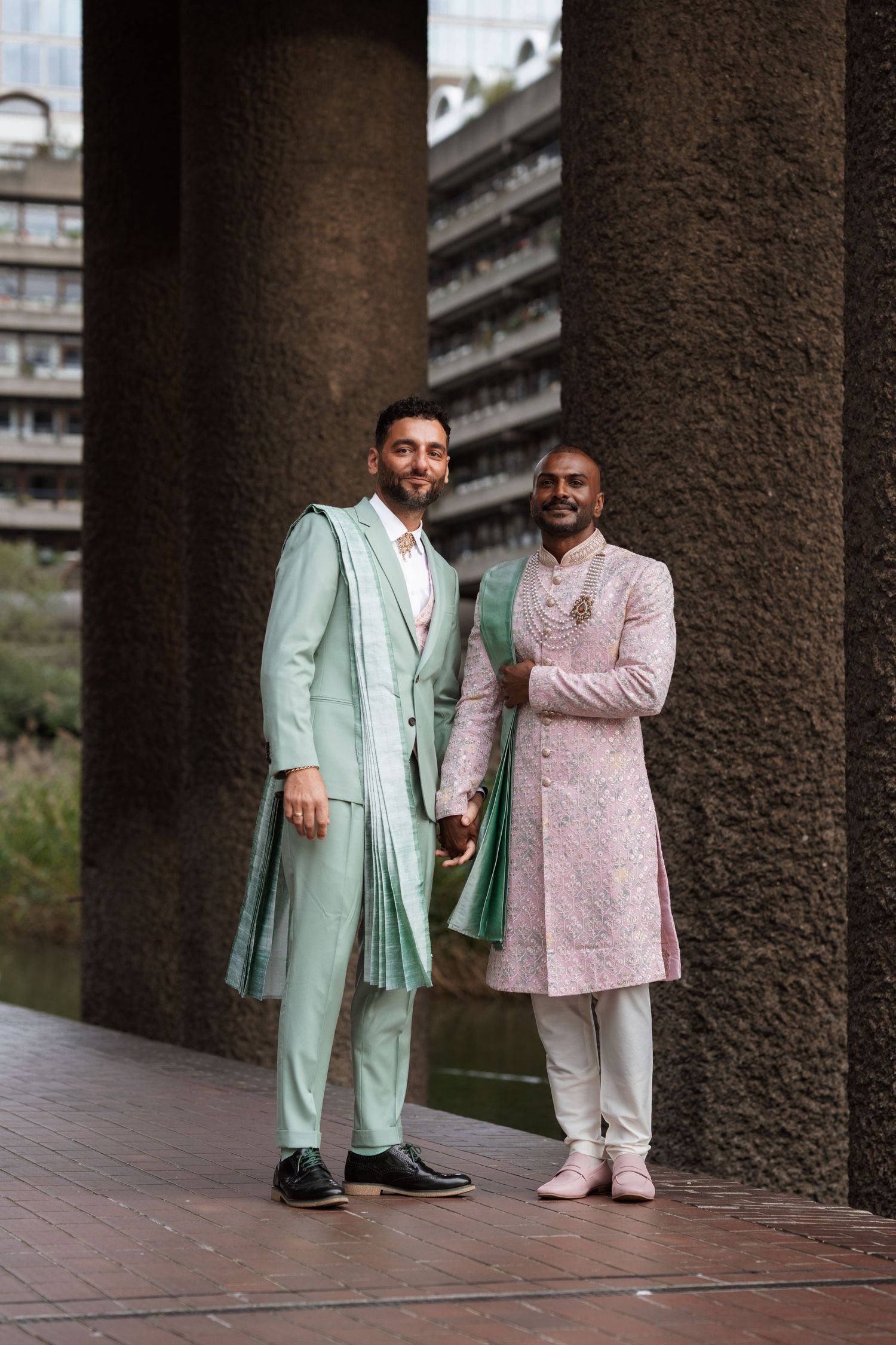 Two people wearing pastel mint and pink formal suits standing between architectural columns.