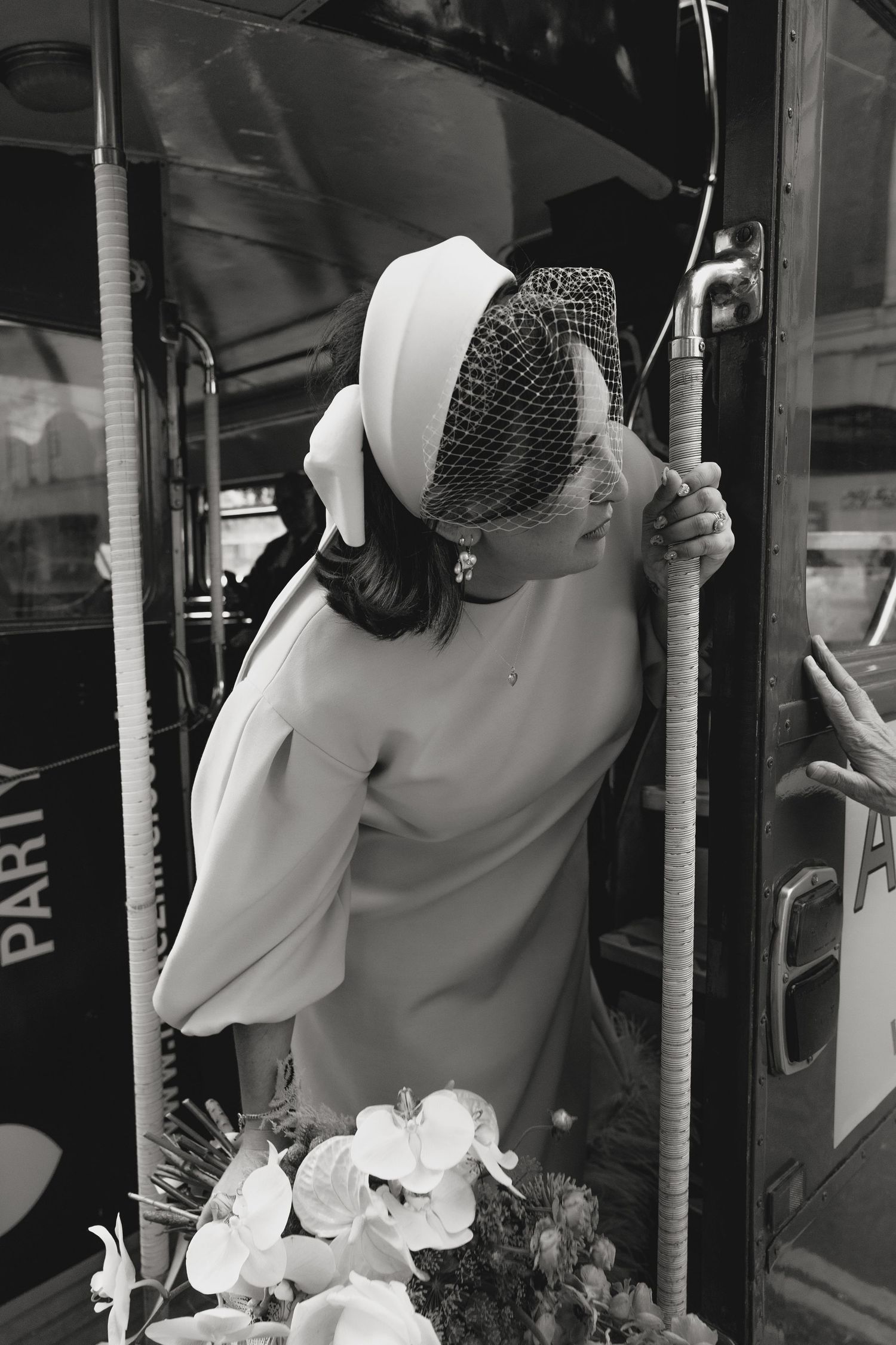 A person in vintage-style dress and headpiece enters a vehicle with flowers.