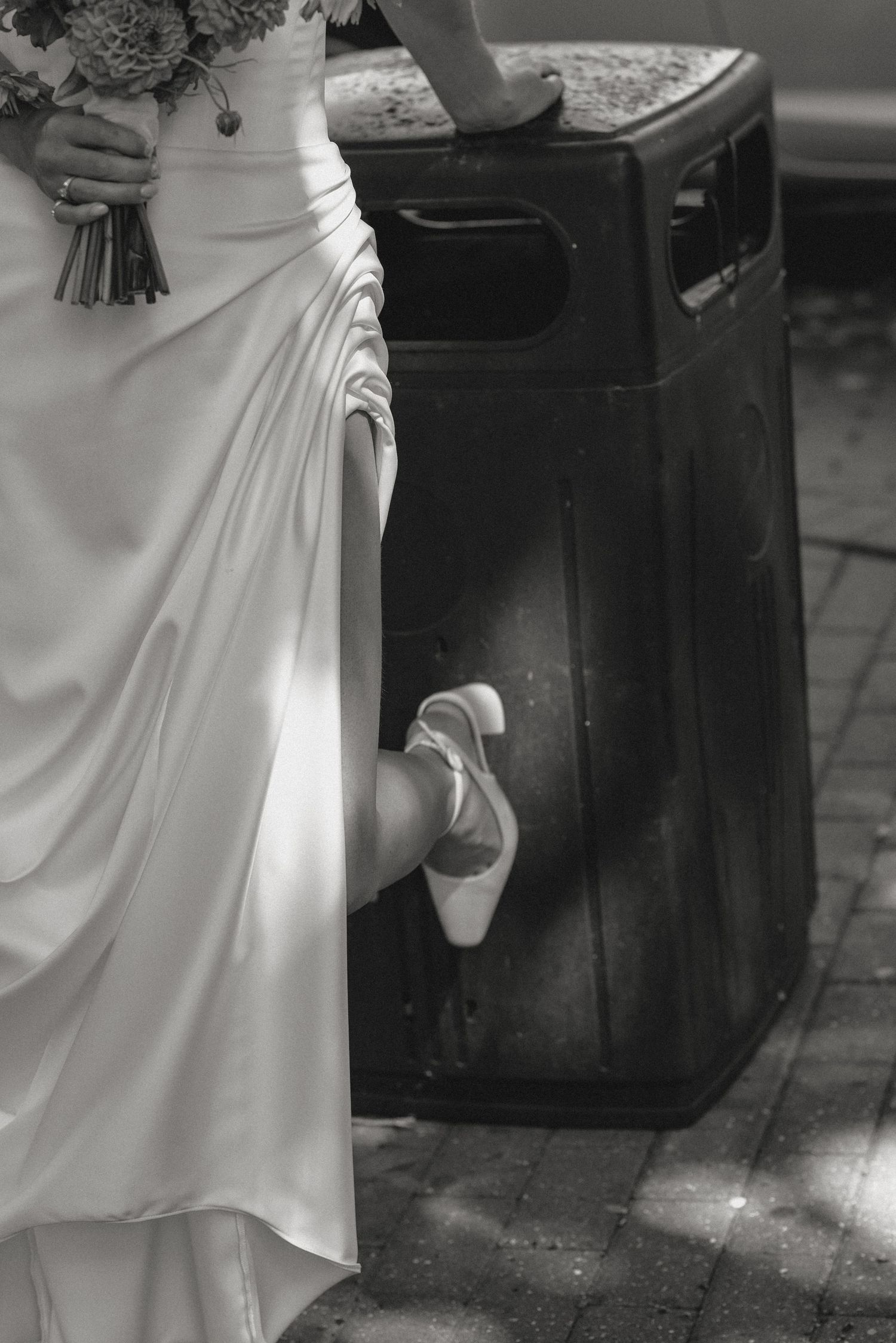 Black and white photo showing the hemline and shoes of a bride in a flowing white gown.