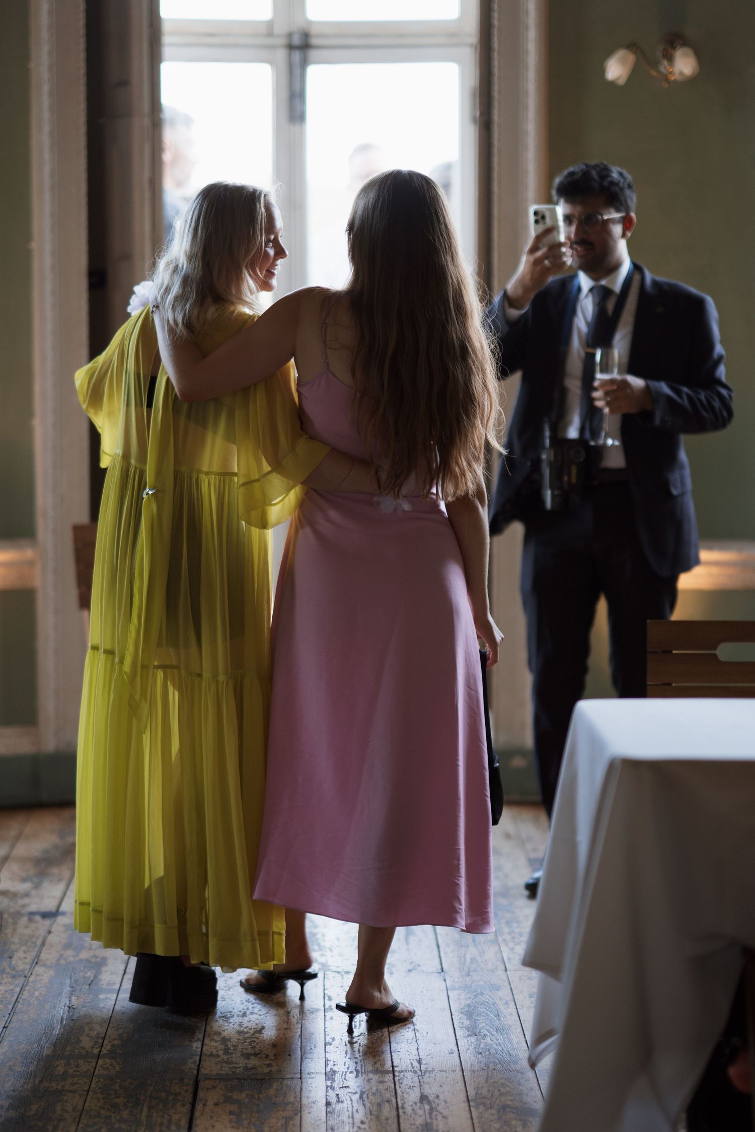 Wedding guests in colorful dresses mingle during indoor reception.