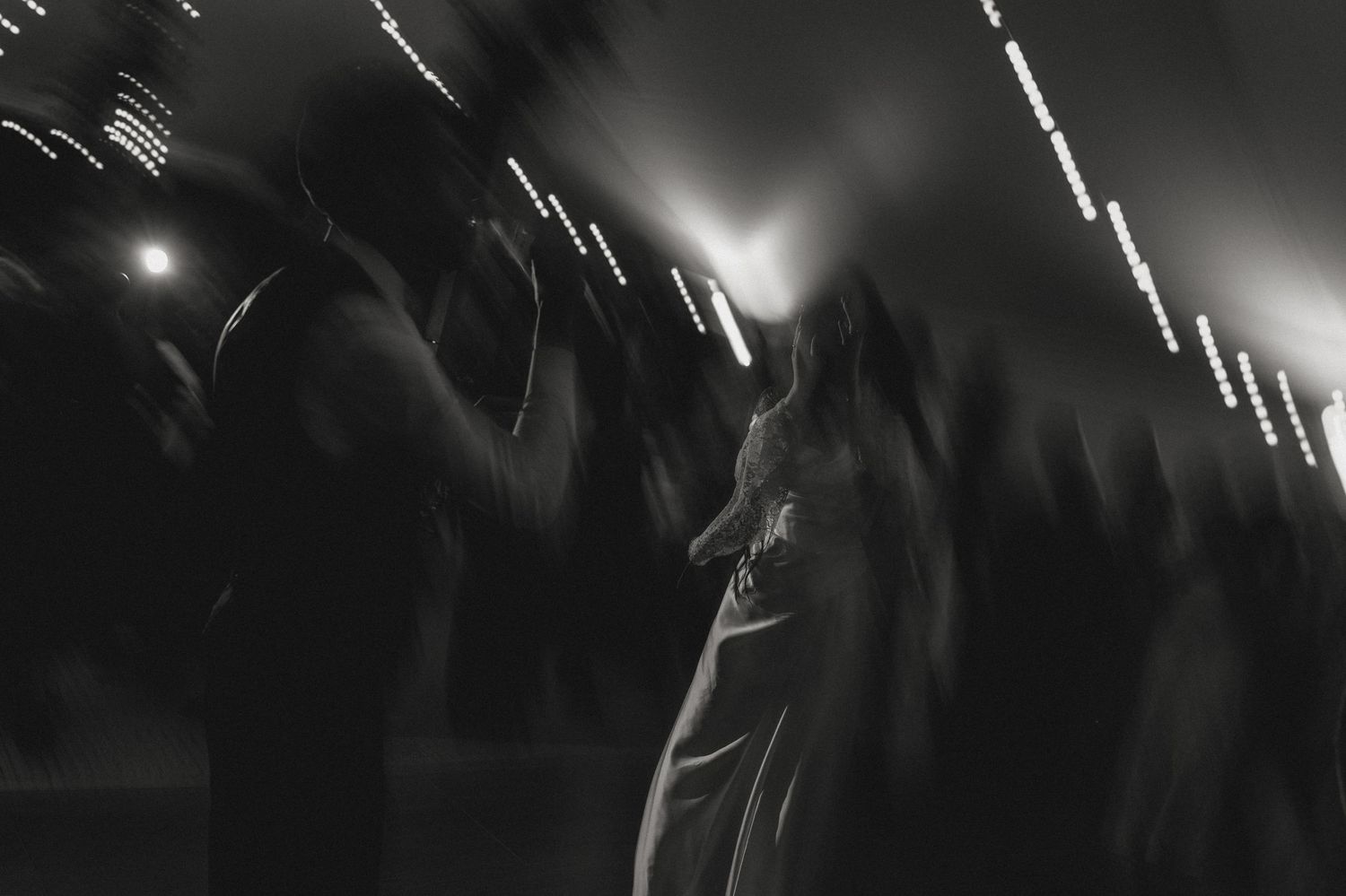 Blurred motion shot of people dancing at a dimly lit wedding reception.