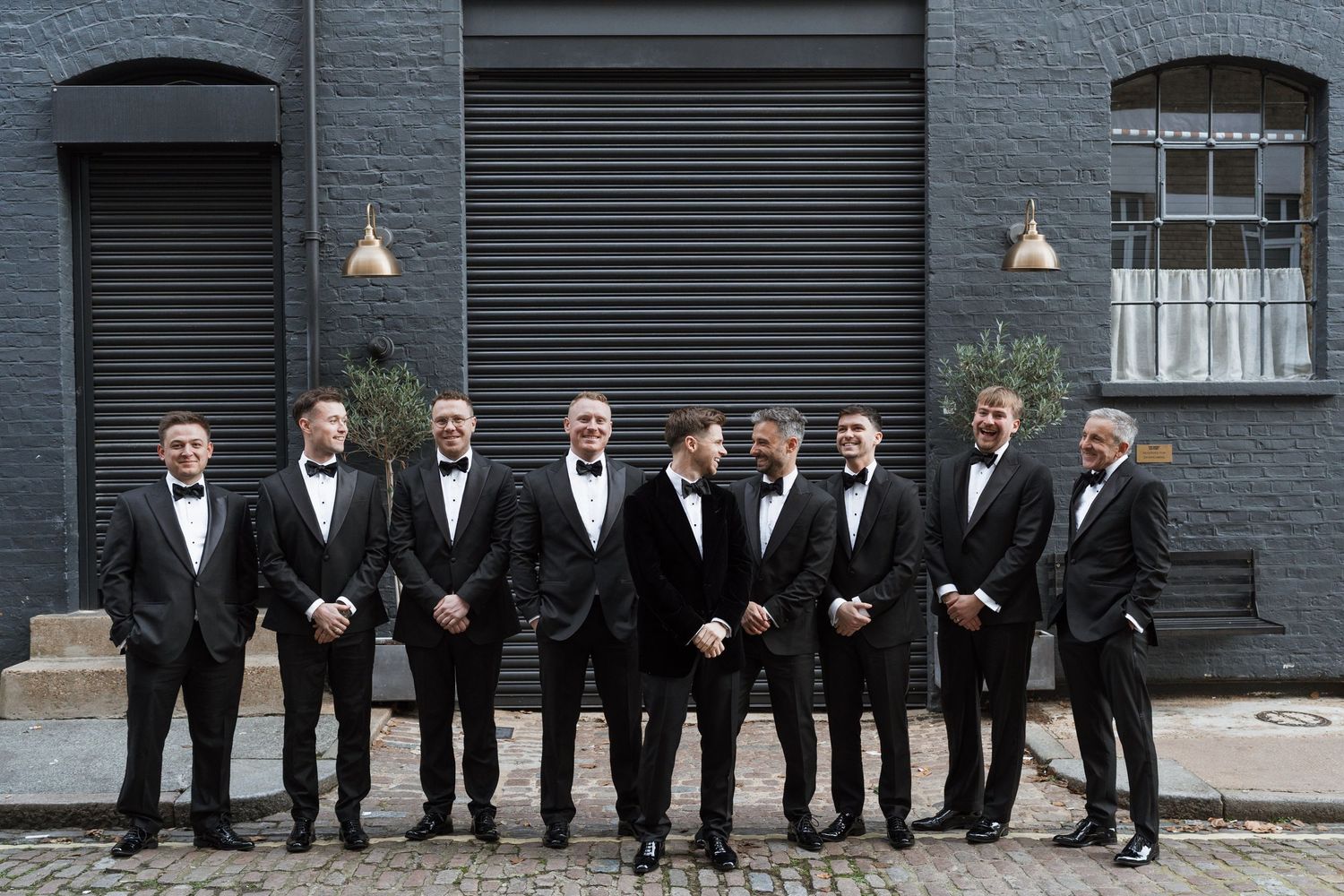A formal group photo of people in black suits lined up against a dark gray wall.