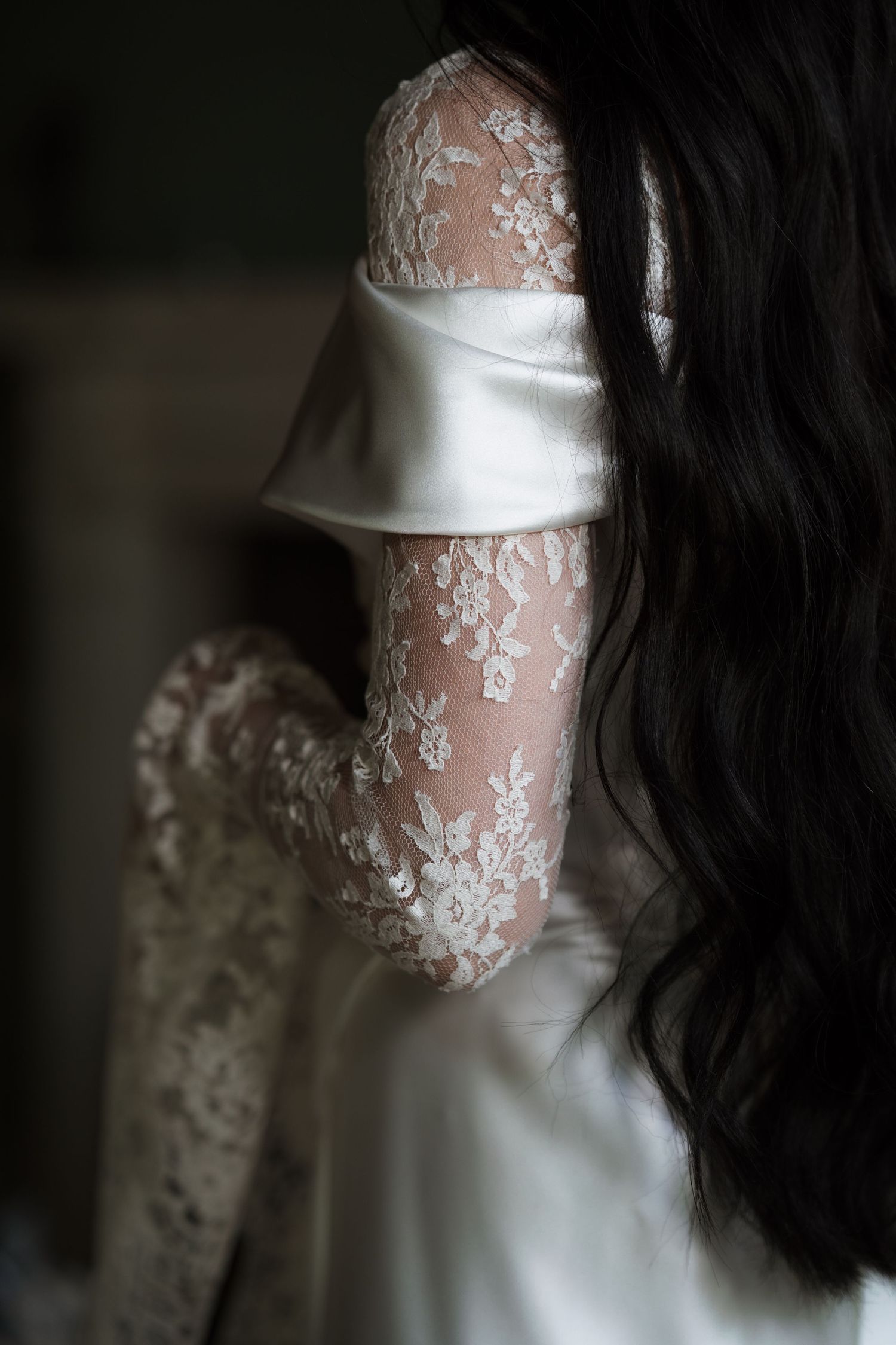 Close-up detail of white wedding dress showing intricate lace pattern and satin fold.