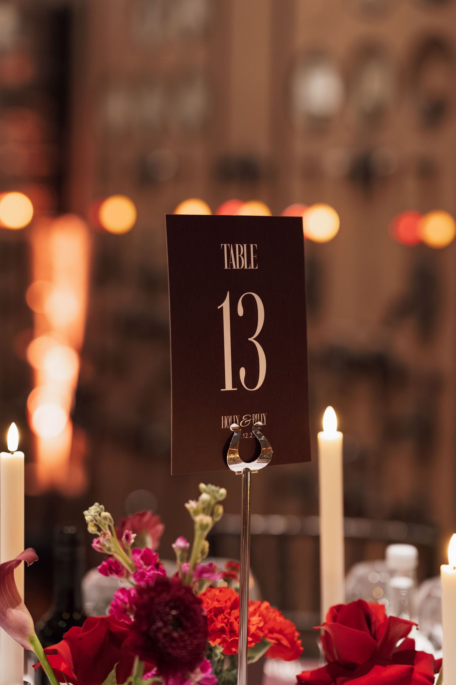 Elegant wedding table setting with red flowers, candles and table numbers in moody lighting.