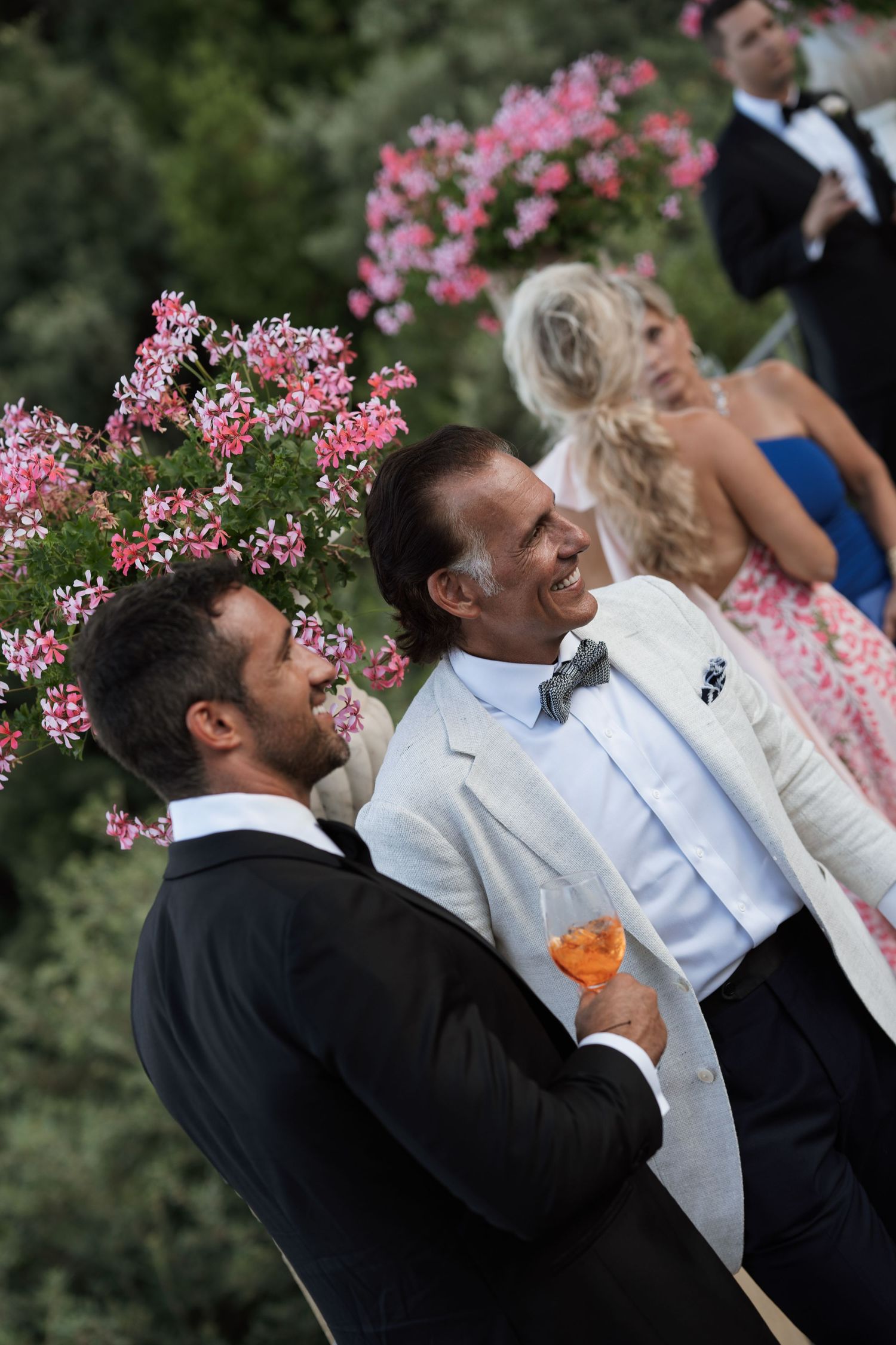 Wedding guests enjoying drinks against backdrop of pink flowers at outdoor reception.