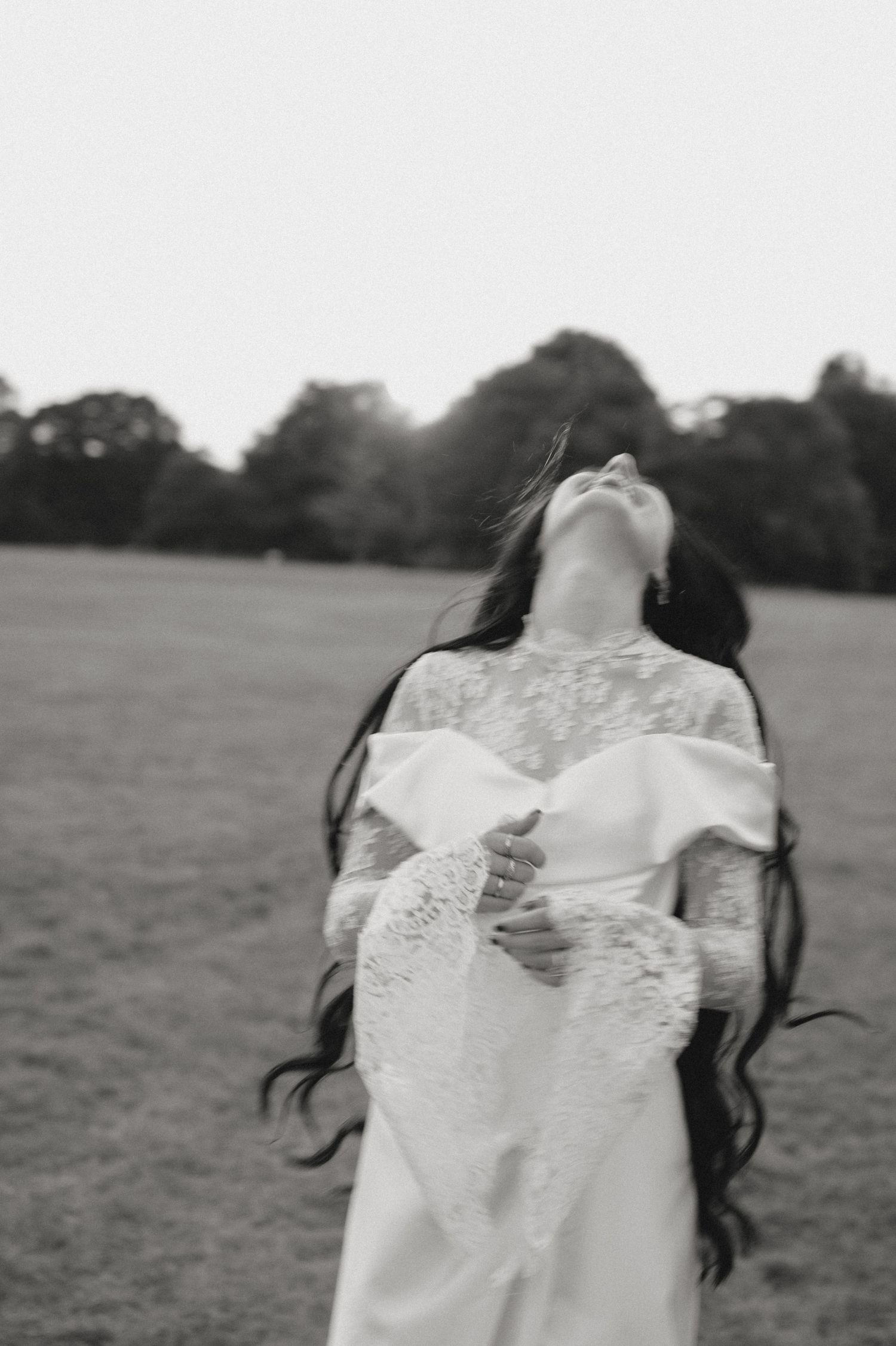Artistic black and white shot of a bride with flowing dark hair in a field.
