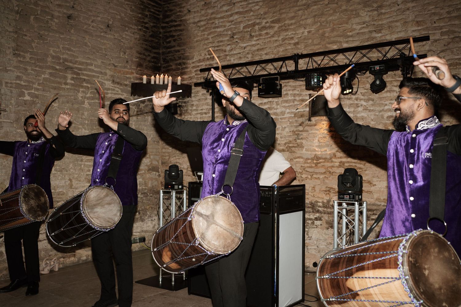 Row of musicians playing traditional drums at brick-walled venue.