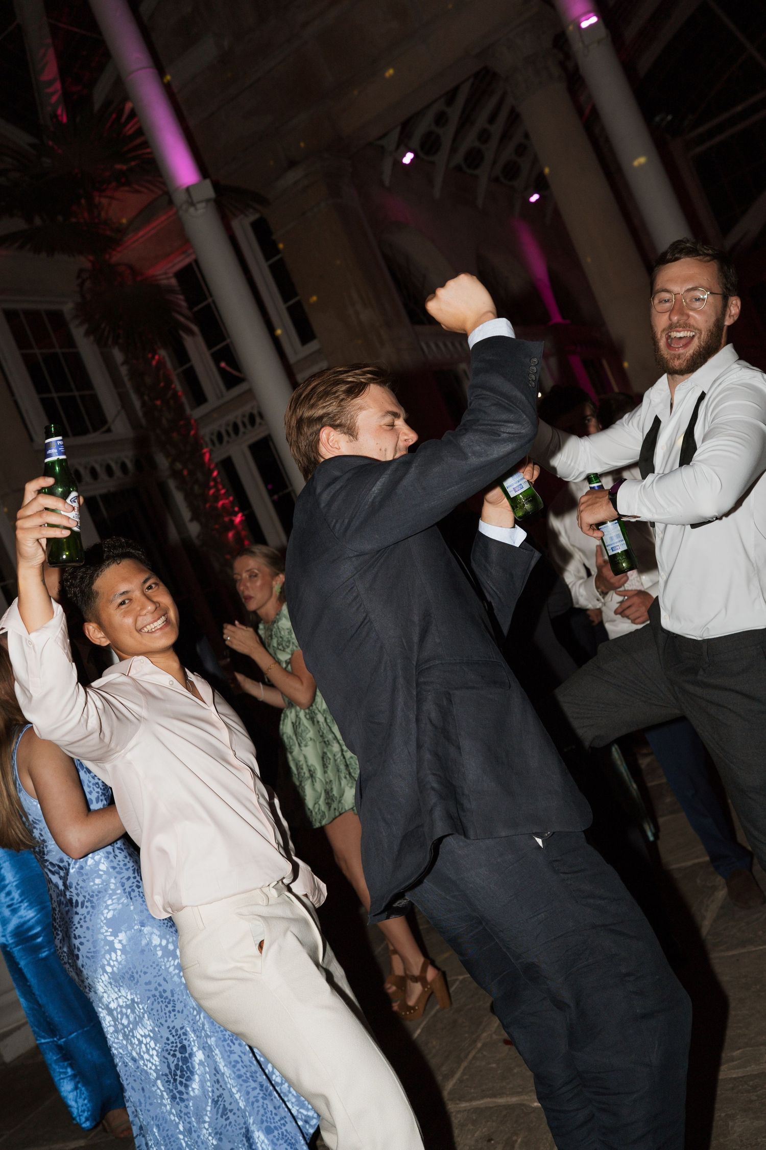 Wedding guests dancing and celebrating on a lively reception dance floor with purple lighting.