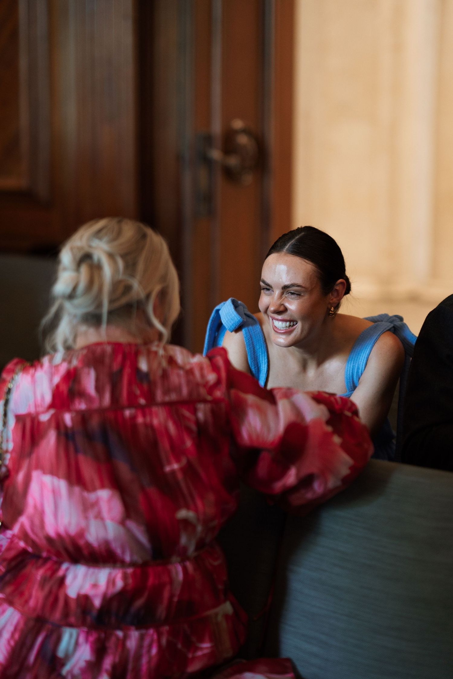 Two guests in colorful dresses share a joyful moment at a formal event.