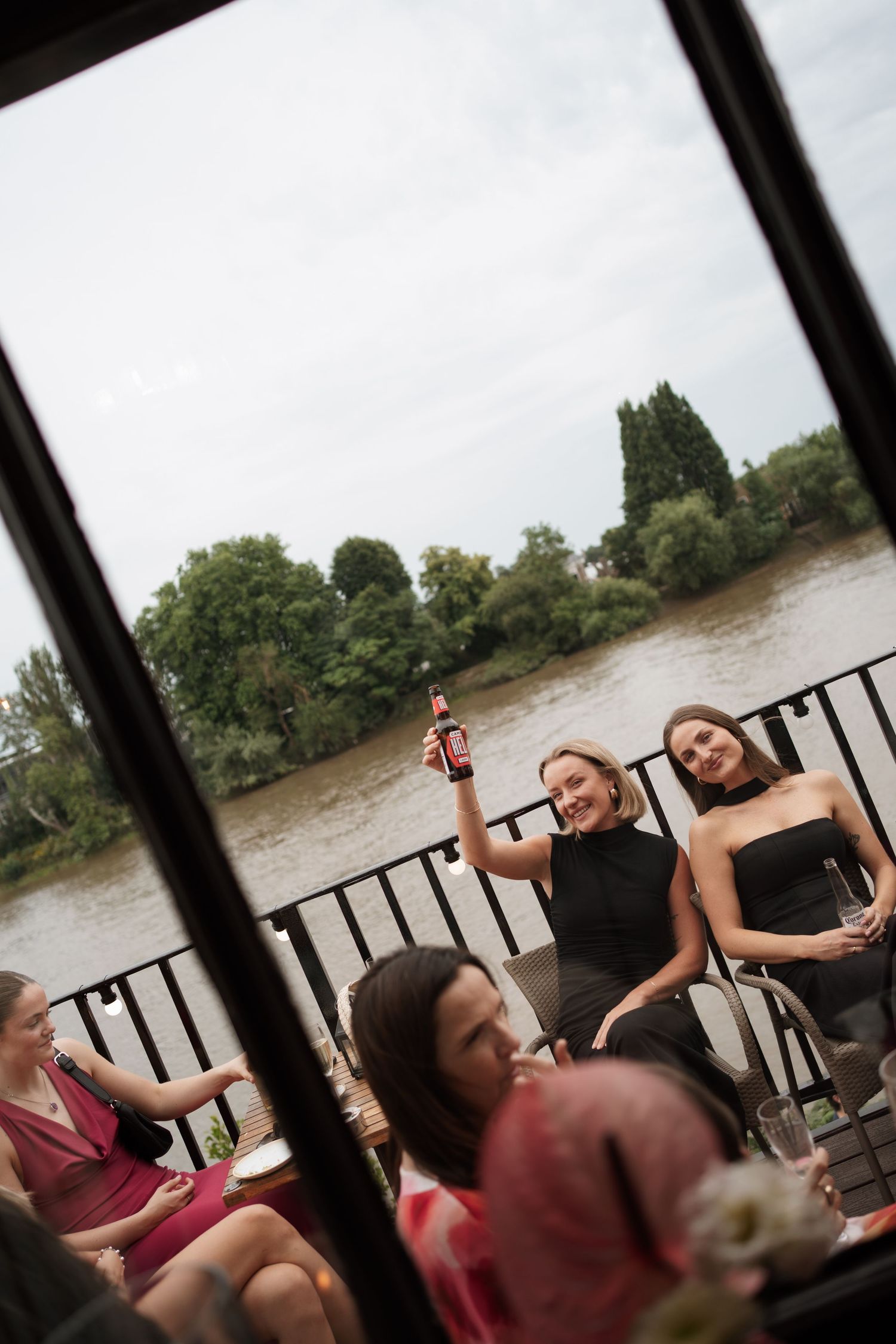 Wedding guests enjoy a lively celebration on an outdoor deck overlooking a river.