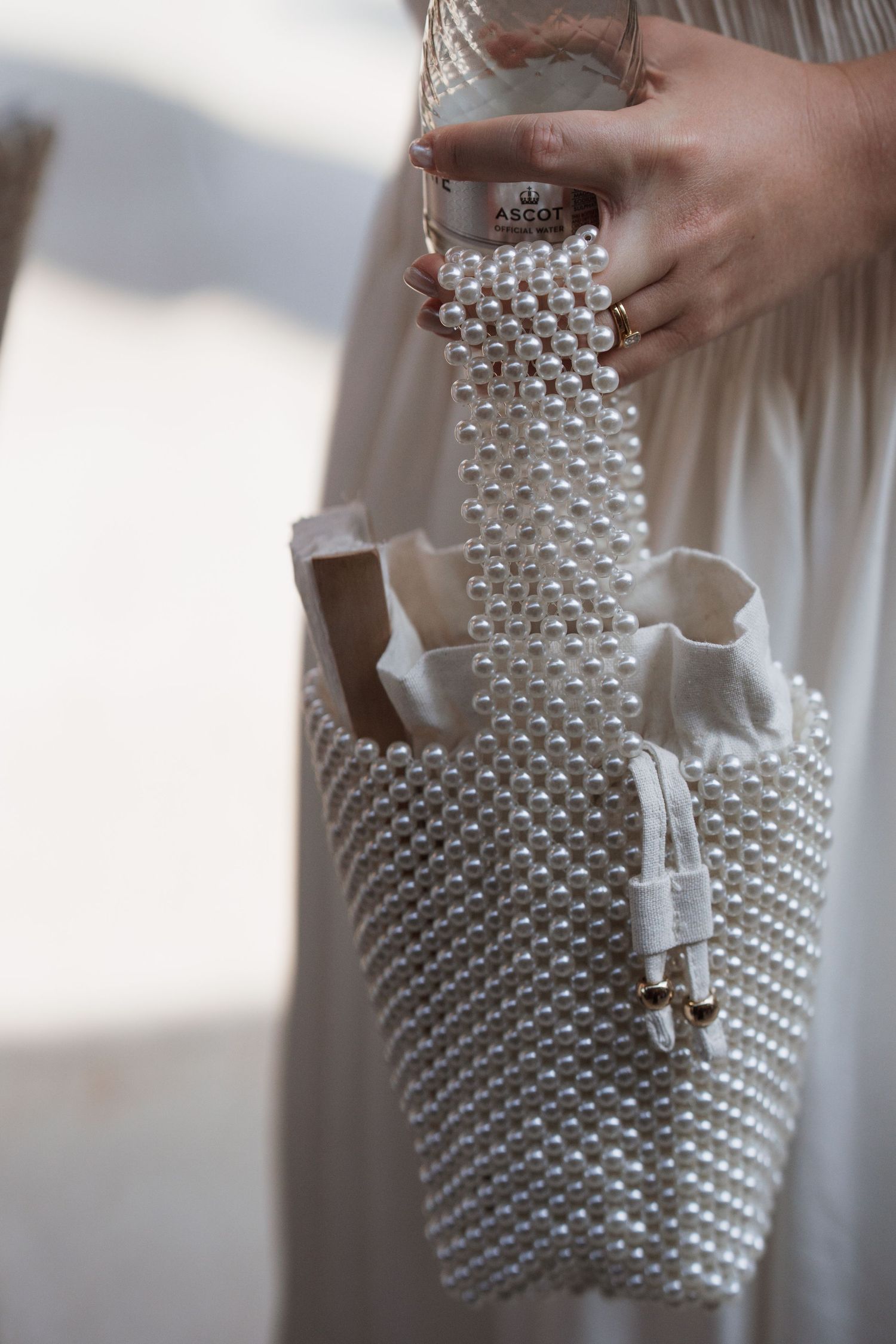 Close-up of hands holding a white beaded handbag with decorative pearl details.
