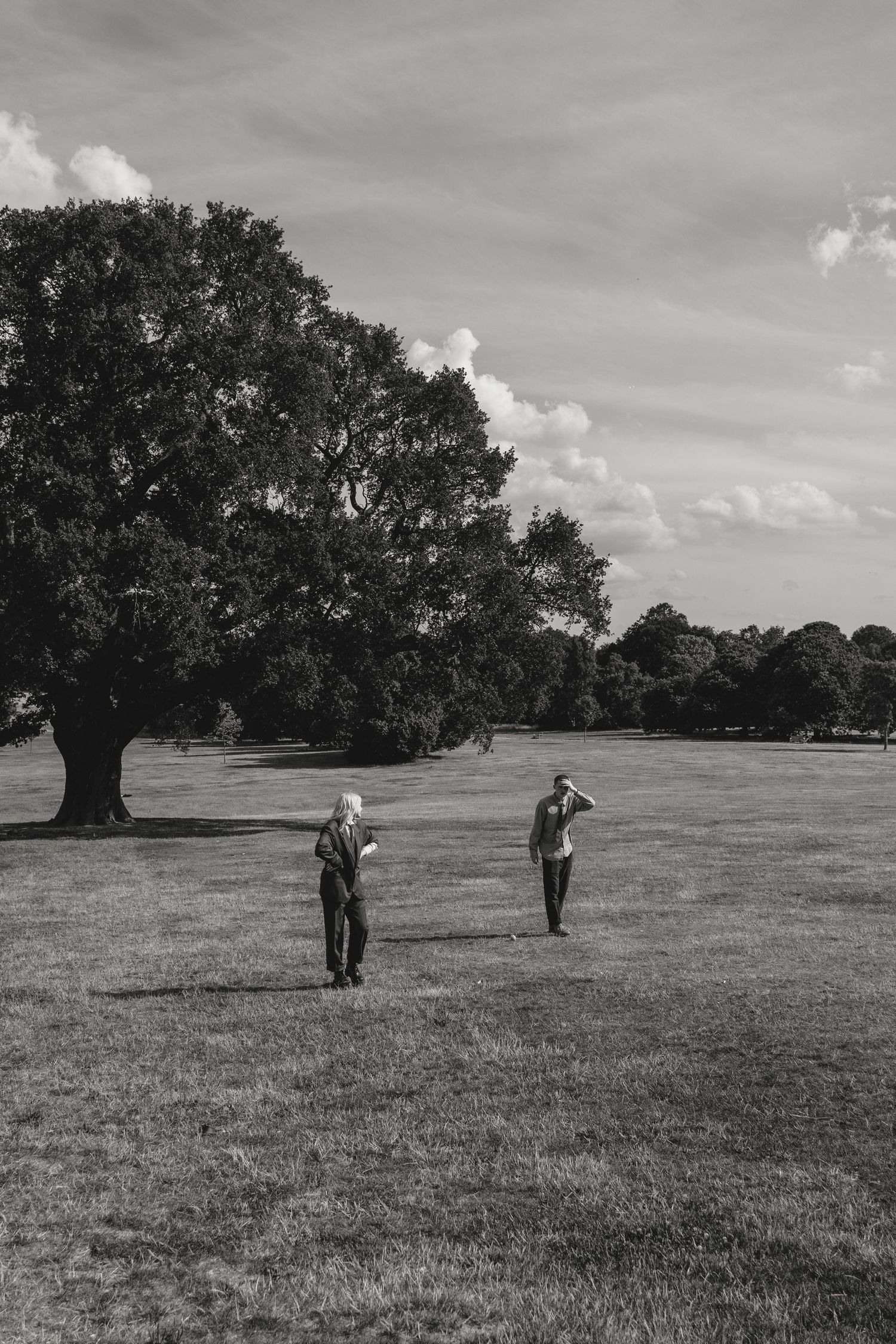 Black and white landscape photo of people walking across a grassy field with large trees.