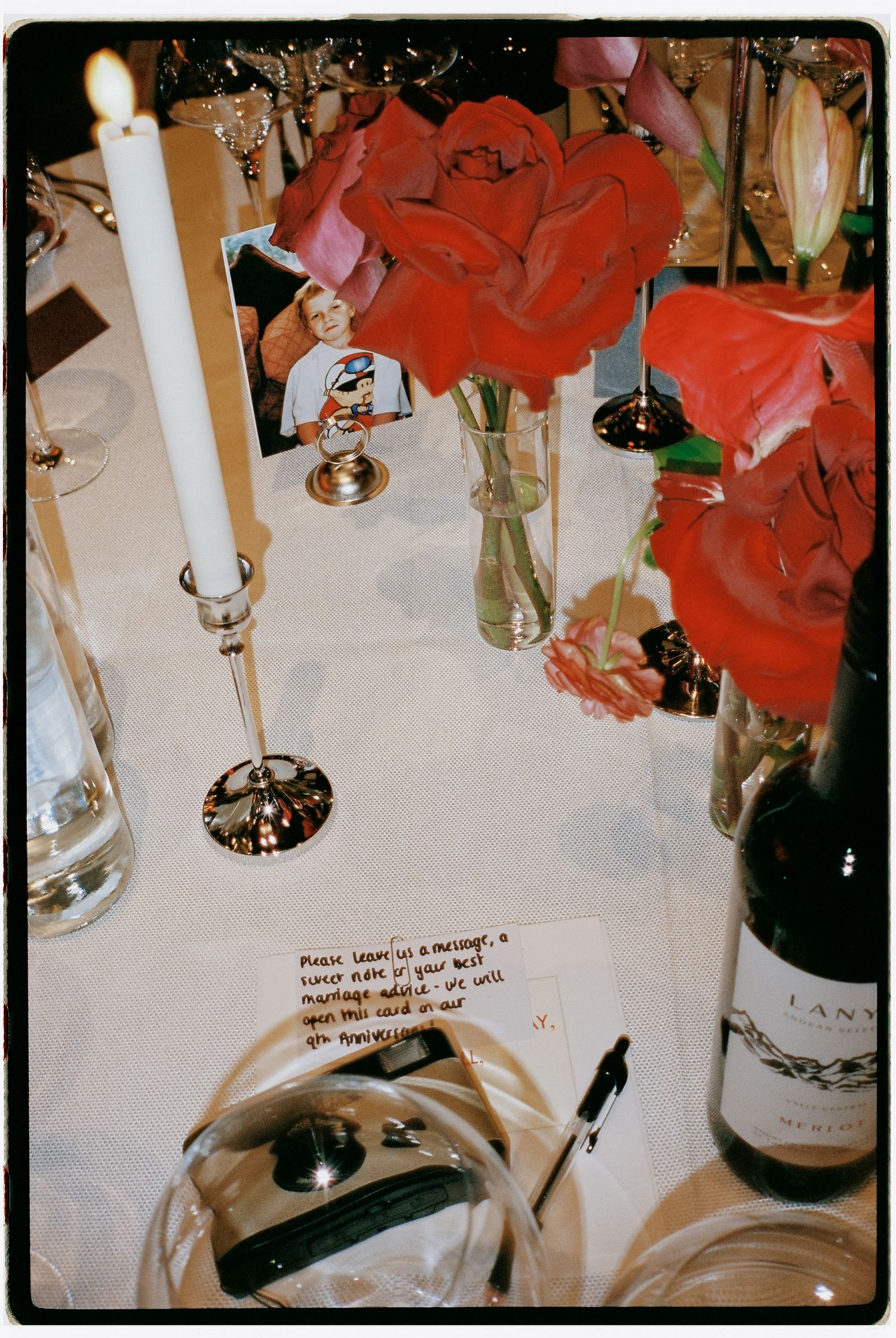 Elegant table setting with red roses, white candles, and wine bottles at a formal dinner.