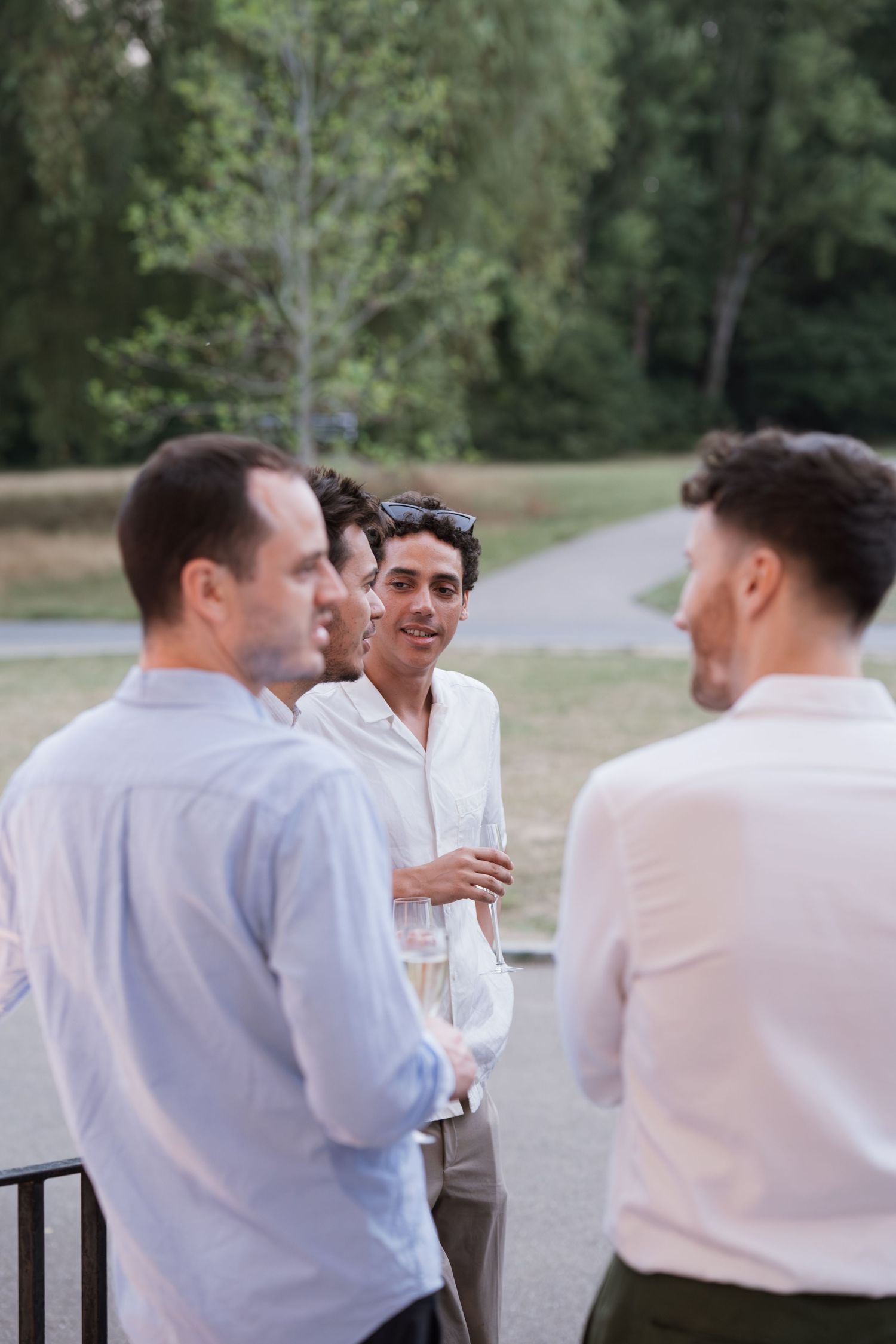 Groomsmen in white shirts chatting outdoors during wedding festivities.