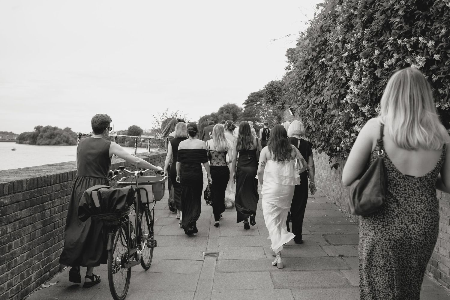 Wedding party members walk along a brick path outdoors.