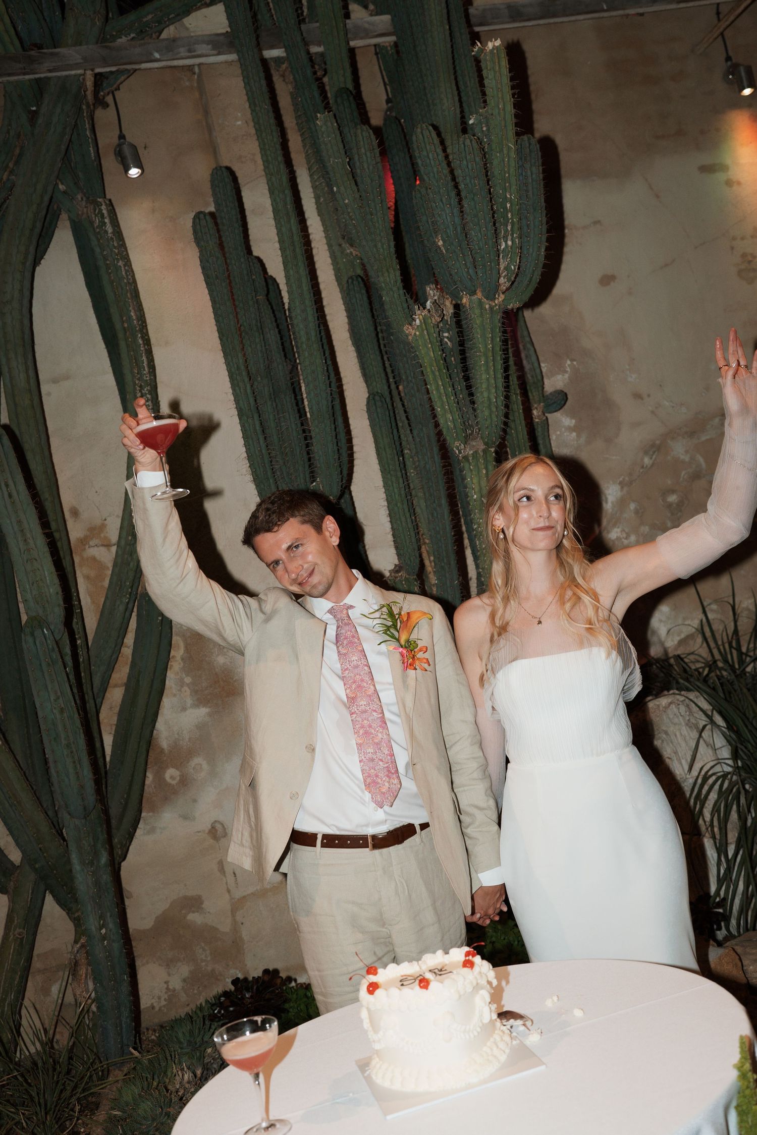 Joyful wedding couple celebrating with cake at a reception surrounded by desert cacti.