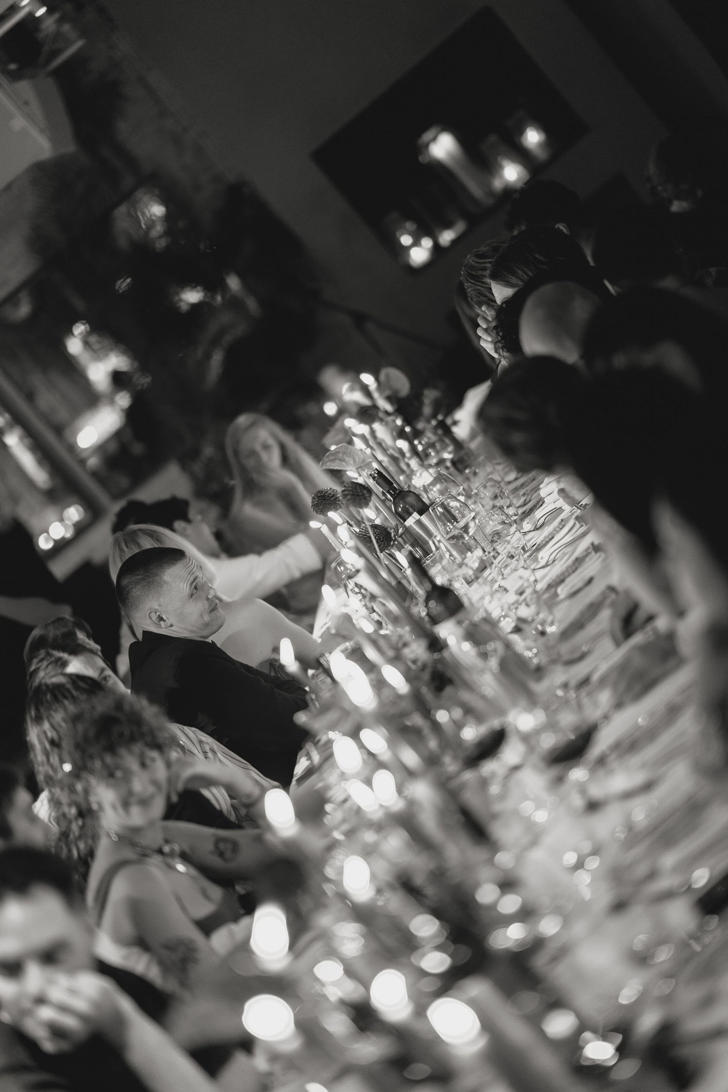 Black and white image of a formal dinner party with glowing candles creating bokeh effects.